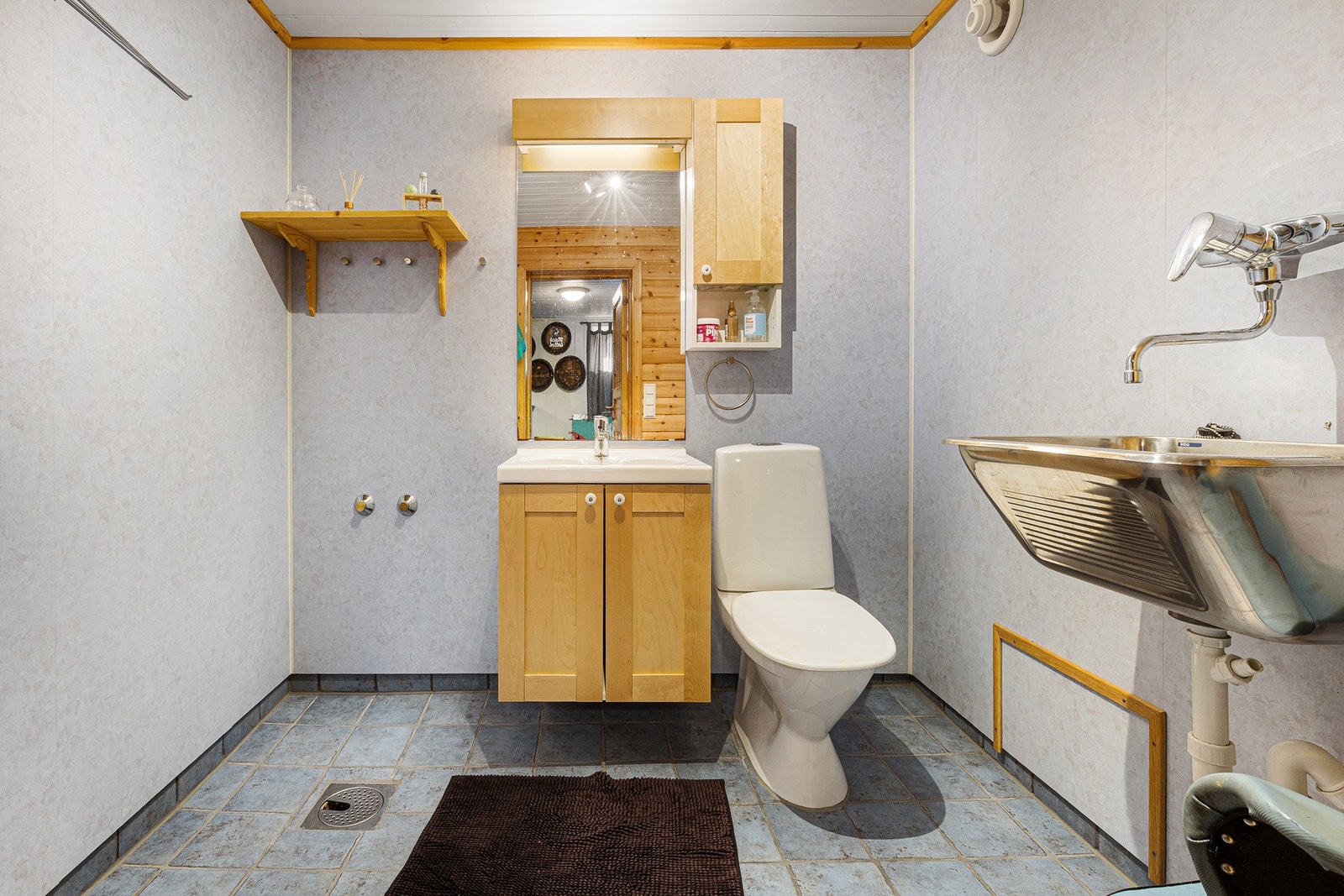 Bad har flislagt gulv og vegger med våtromsplater. Bad har gulvmontert toalett, servant i liten innredning og skyllekar montert på vegg. Galleribilde