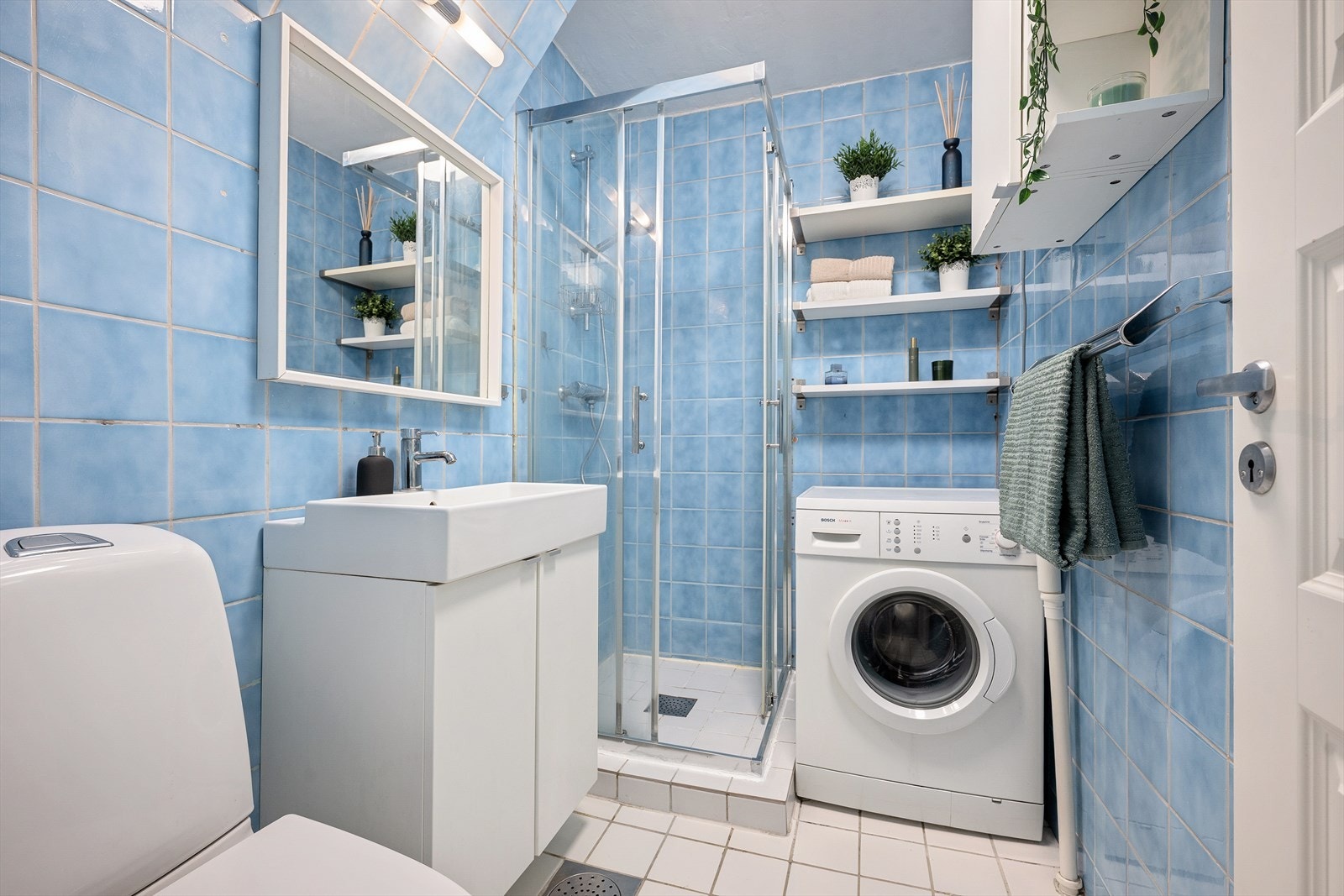 Baderommet er flislagt og har en eldre konstruksjon med dusj, servant, toalett og opplegg for vaskemaskin Galleribilde