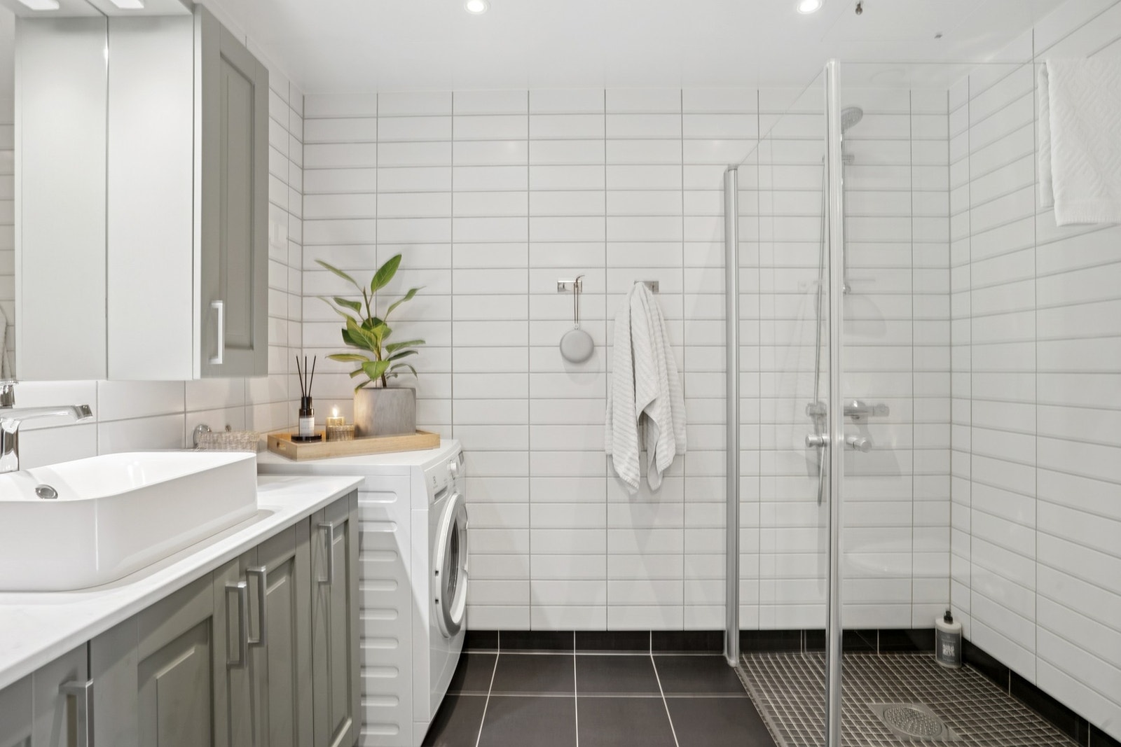 Badet er innredet med lyse fliser, dusjhjørne og opplegg for vaskemaskin, samt god oppbevaringsplass i innredningen. Galleribilde