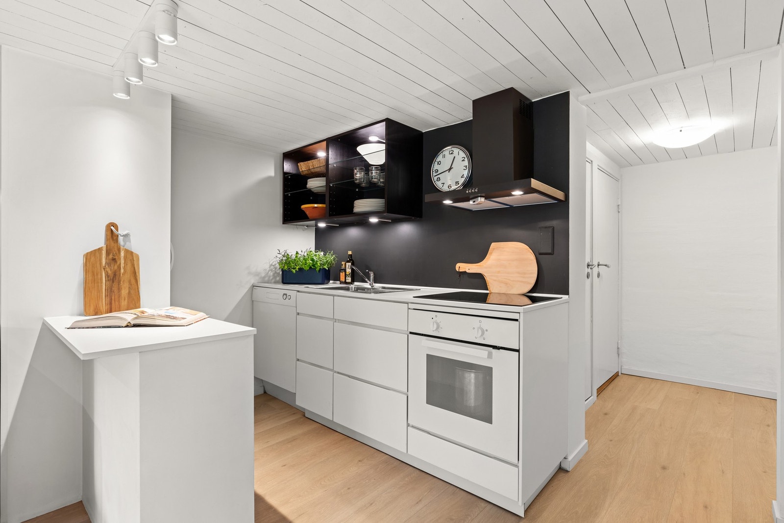 Kjøkkendelen i kjeller er utstyrt med en innredning fra 2018 med glatte hvite fronter og vegghengte hyller i sort. Galleribilde