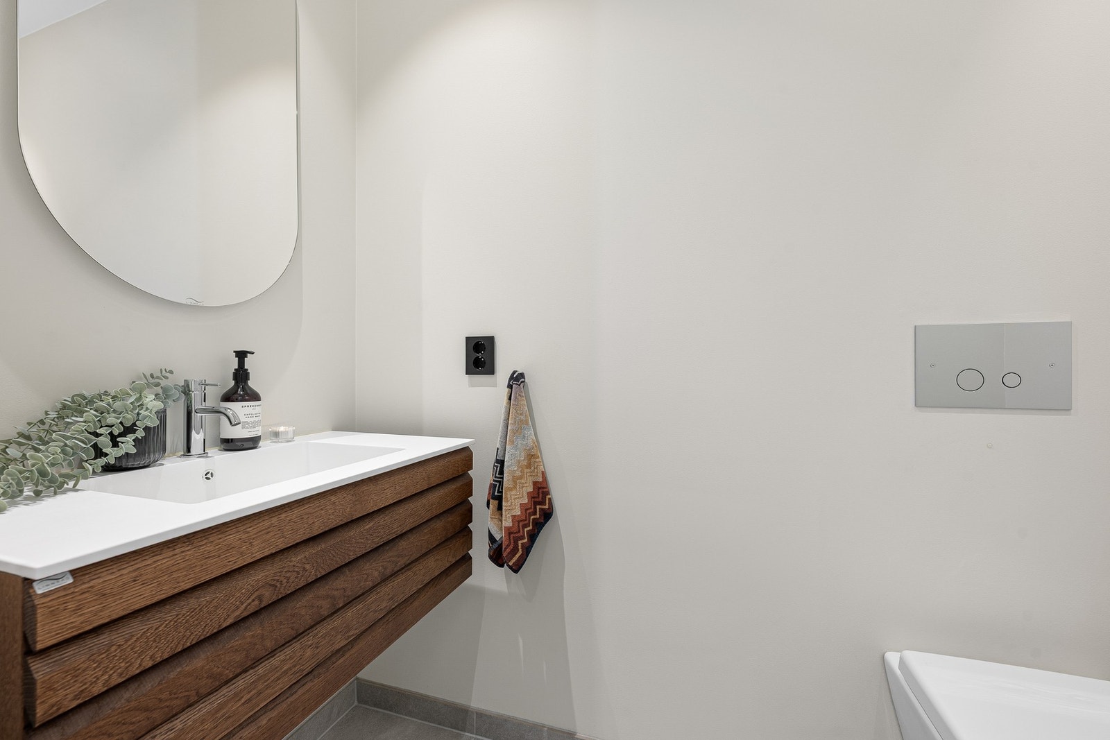 Toalettrommet fremstår moderne og stilrent med gjennomgående kvalitetsmaterialer. Rommet er innredet med vegghengt servantinnredning fra Linn Bad i mørk eik, kombinert med en elegant Corian topplate. Galleribilde