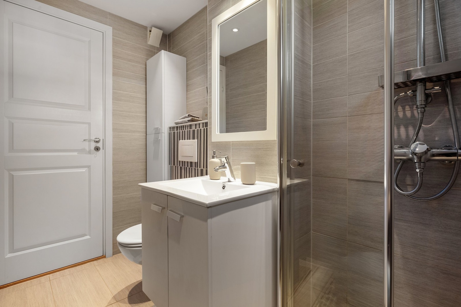 Badet er innredet med vegghengt toalett, dusjvegger som kan foldes sammen og dusjgarnityr, samt baderomsinnredning med servant og speil. Galleribilde