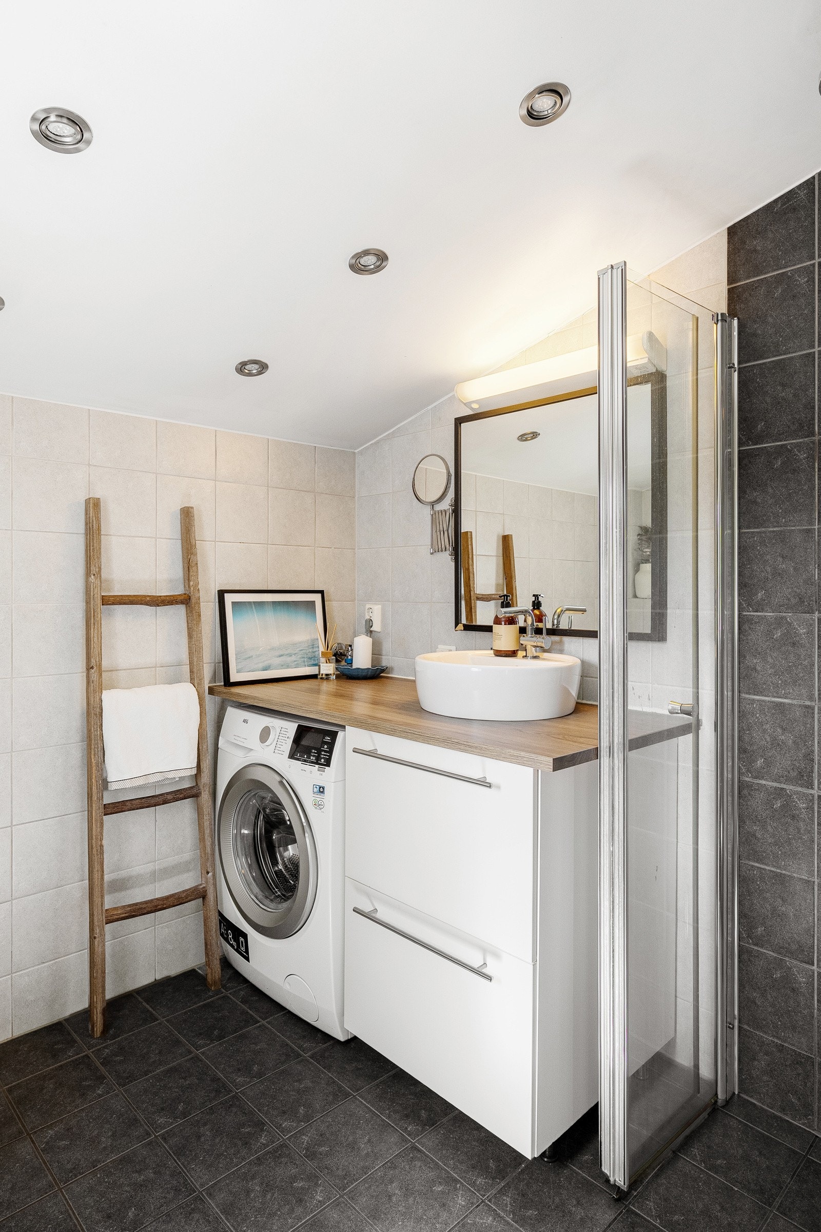 Baderomsinnredningen består av seksjon med vask, speil med belysning, opplegg for vaskemaskin, dusjhjørne og vegghengt toalett. Galleribilde