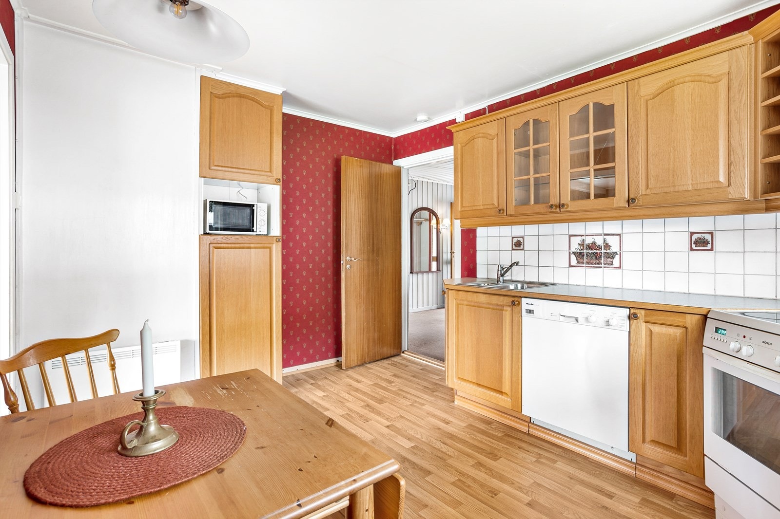 Innredningen har en funksjonell L-form og profilerte eikefronter, vitrineskap og laminatbenkeplate med dobbel oppvaskkum i metall. Galleribilde