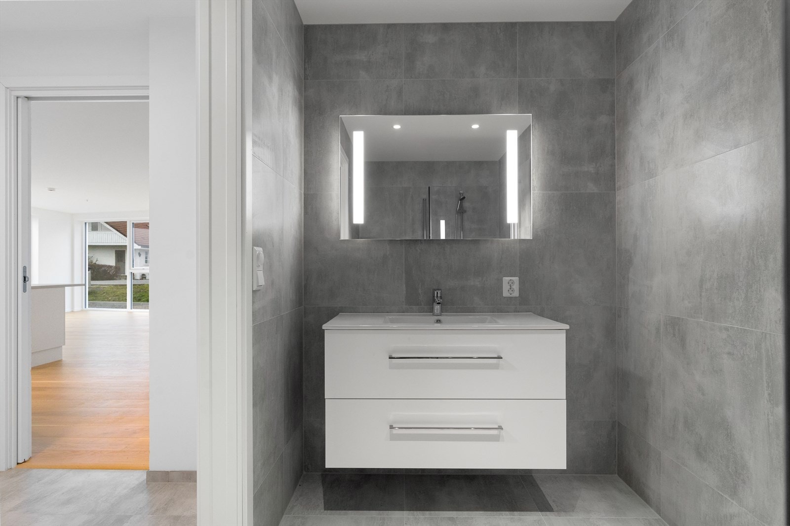 Baderommet er fullfliset og utstyrt med gulvvarme for ekstra komfort. Dusjnisjen har glassvegger som gir et elegant preg Galleribilde