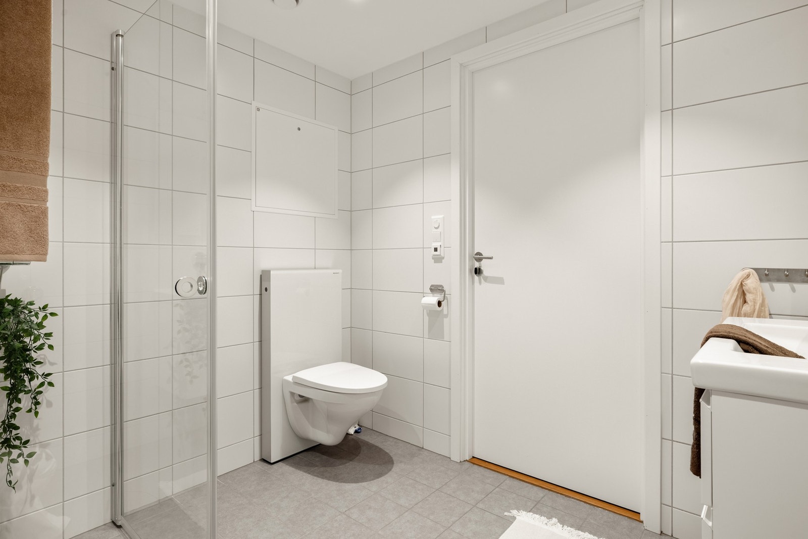 Det er helfliset og har en slett malt himling med innfelte downlights i himling og varmekabler i gulv. Badet er innredet med dusj m/glassvegger, vegghengt toalett, baderomsinnredning og opplegg for vaskemaskin. Galleribilde