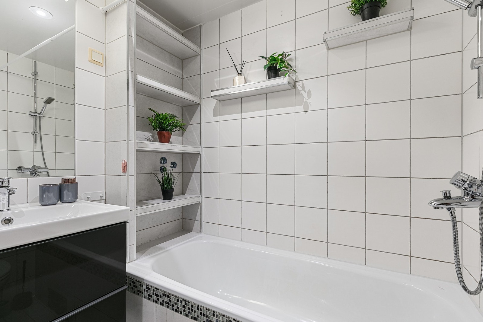 Innredningen består av badekar med dusjgarnityr, veggmonterte hyller og praktisk oppbevaringsløsning, servant med underskap og speil med lys Galleribilde