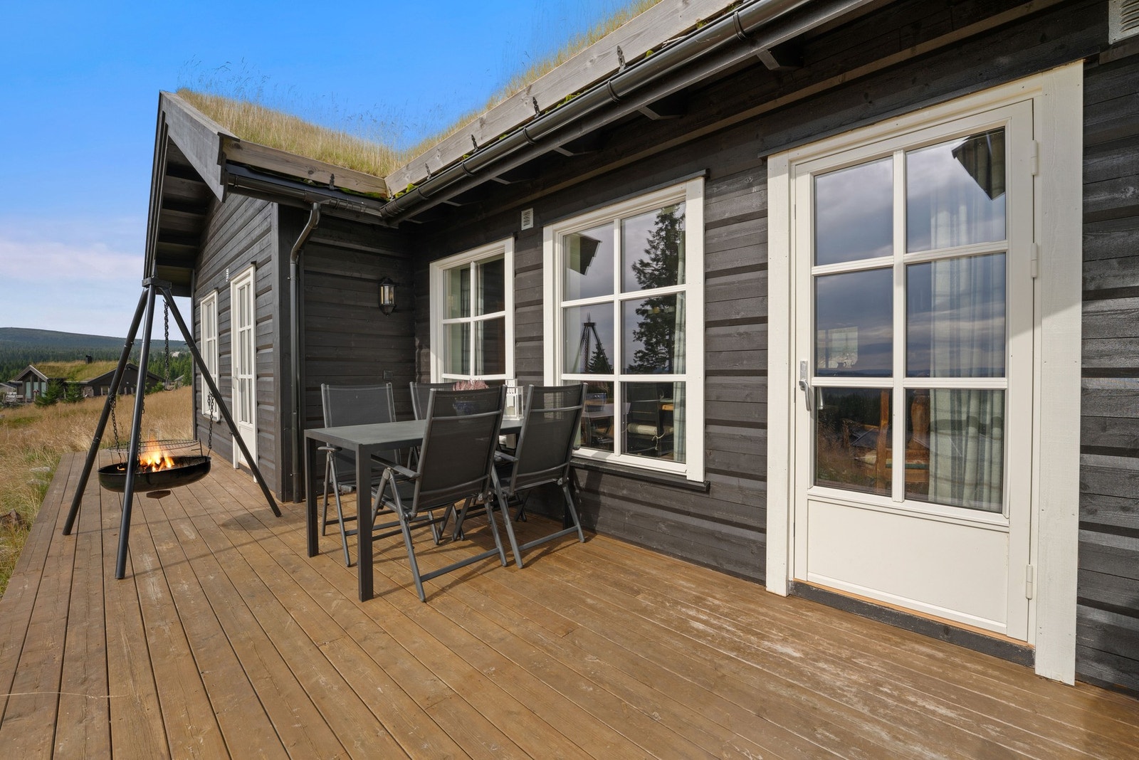 Solrik terrasse med sitteplasser og bålpanne. Hytta har store vinduer som slipper inn mye lys. Flott utsikt over snødekt landskap og skog. Galleribilde