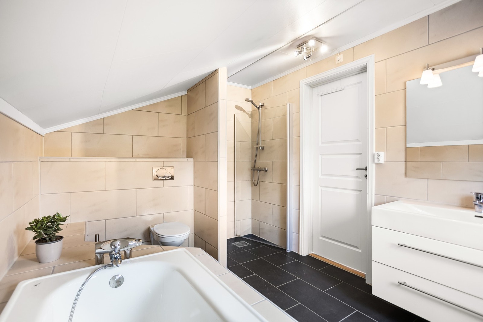 Badet er fra byggeåret 2006 romslig og holdt i en tidløs stil med sorte gulvfliser med gulvvarme og lysbeige fliser på vegg. Galleribilde