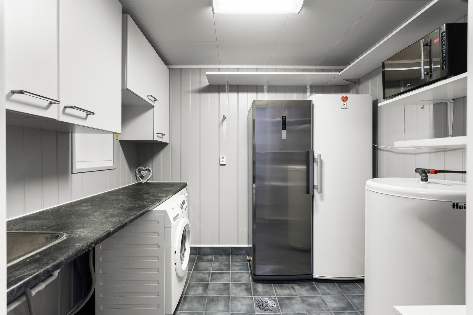 Vaskerom fra byggeåret 2006 innredet med hvite skap over og under en funksjonell arbeidsbenk med utslagsvask. Under benken er det også opplegg for vaskemaskin og tørketrommel. Galleribilde