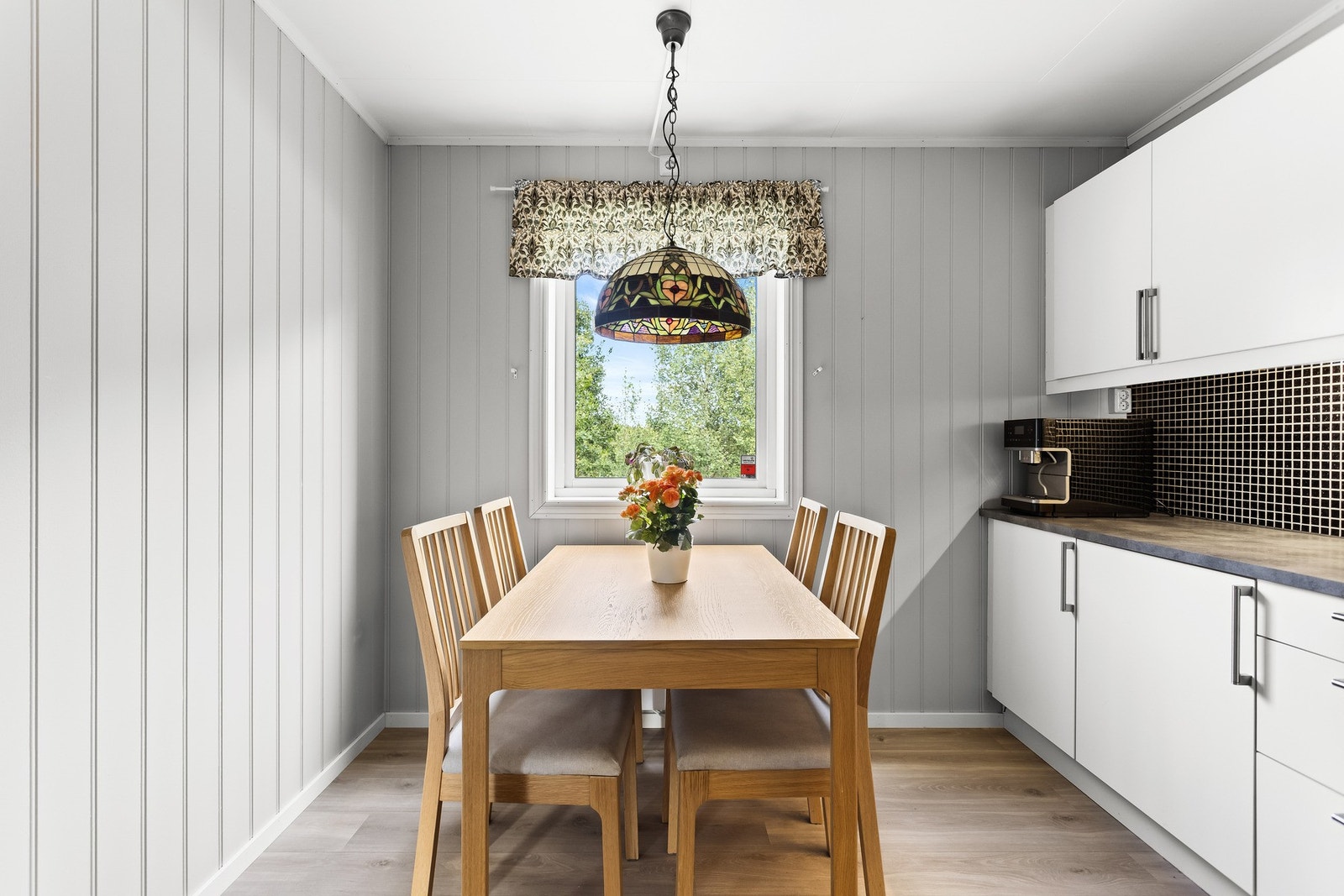 Kjøkkenet har veggpanel i dus farge og plass til et hyggelig spisebord ved vinduet. Galleribilde