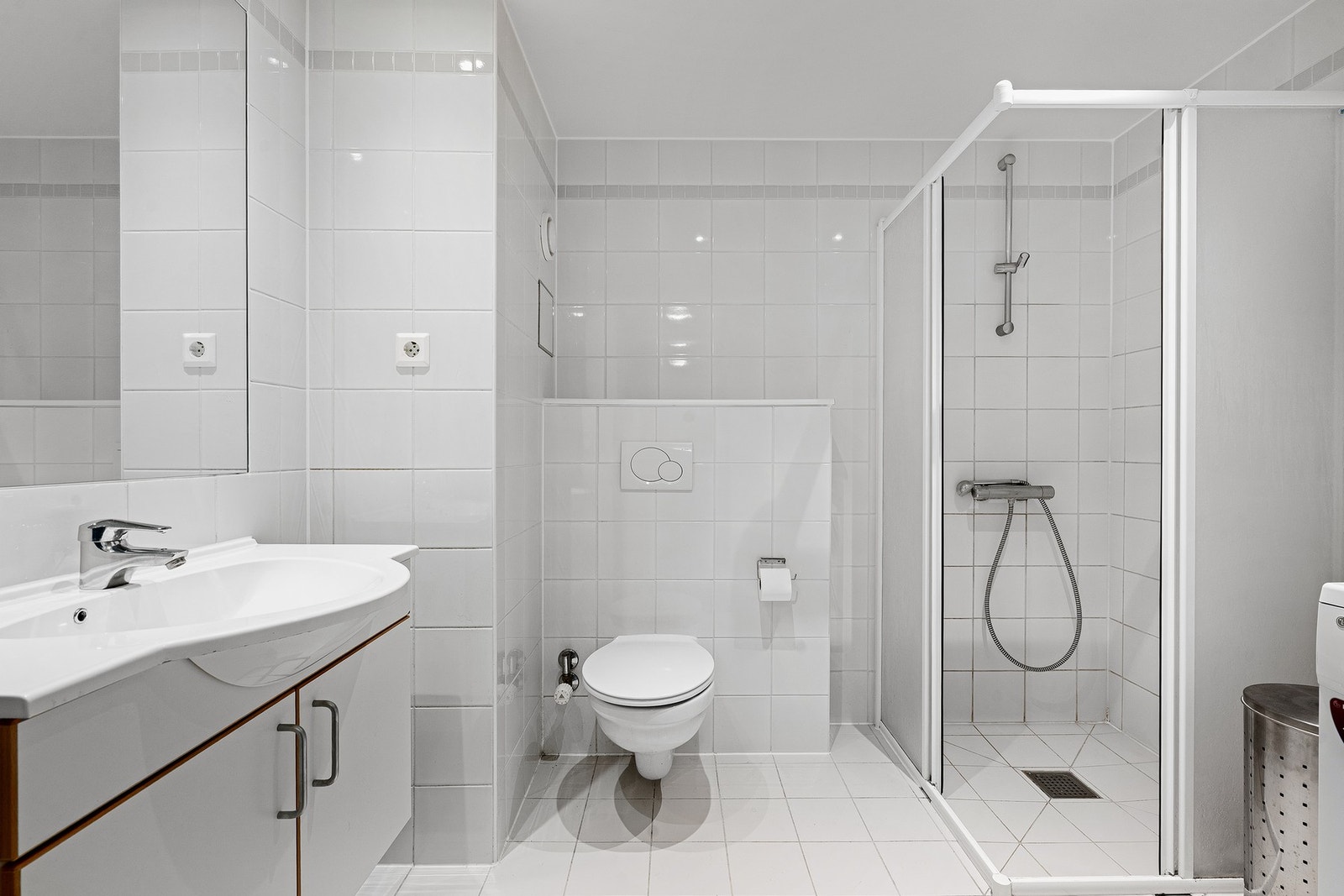 Tidløst, helfliset bad med romslig dusjhjørne og opplegg for vaskemaskin. Galleribilde