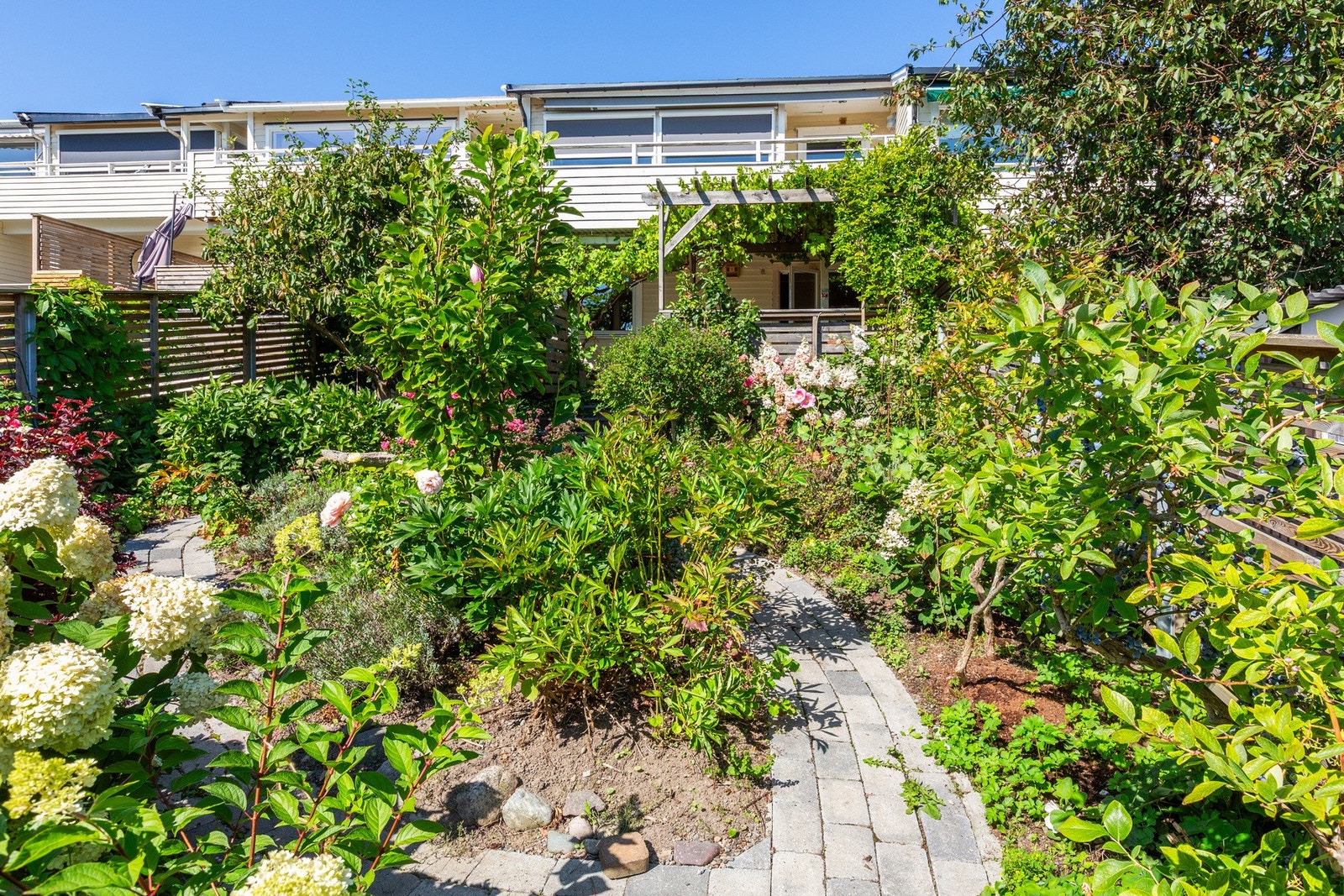 Hagen er delt i felter med steinlagte gangveier. Den passer seg stort sett selv, beplantet med voksende hortensiaer, magnoliaer, rhododendron og blåbærtrær. På veranda er det pergola med blåregn og drue som skaper sydlandsk stemning. Galleribilde