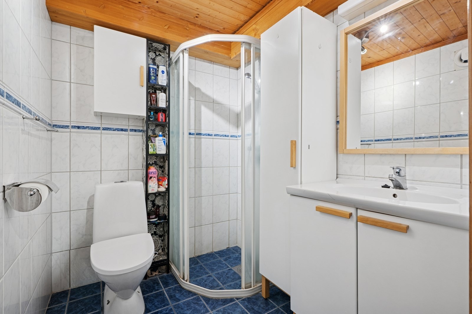Badet er utstyrt med baderomsinnredning med servant og blandebatteri, speil, lys, gulvstående toalett og dusjhjørne med glassdører. Galleribilde