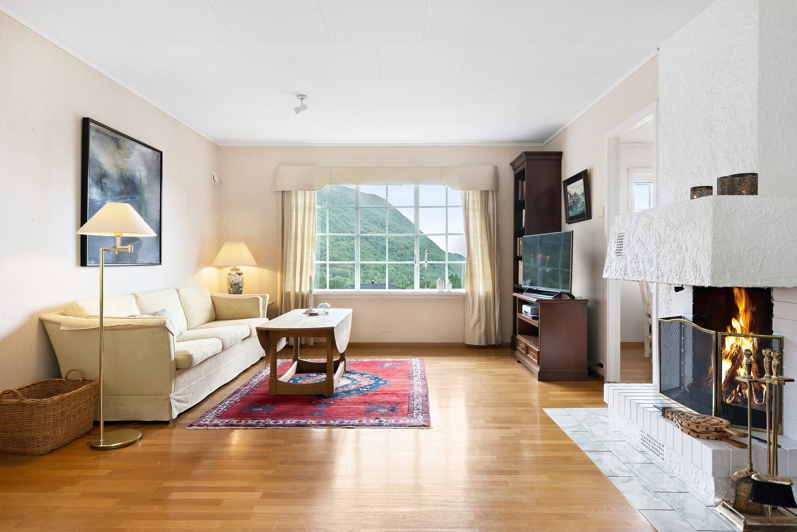 Stua som er i vinkel, har åpen peisinnsats og parkettgulv. Galleribilde