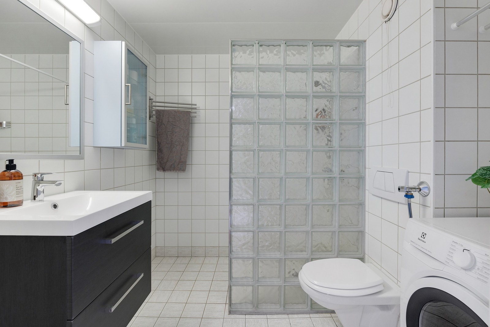 Pent flislagt bad. Innredningen er bestående av servant med underskap, høyskap, speil
med lys over,veggmontert toalett med innebygget sisterne og opplegg for vaskemaskin. Galleribilde