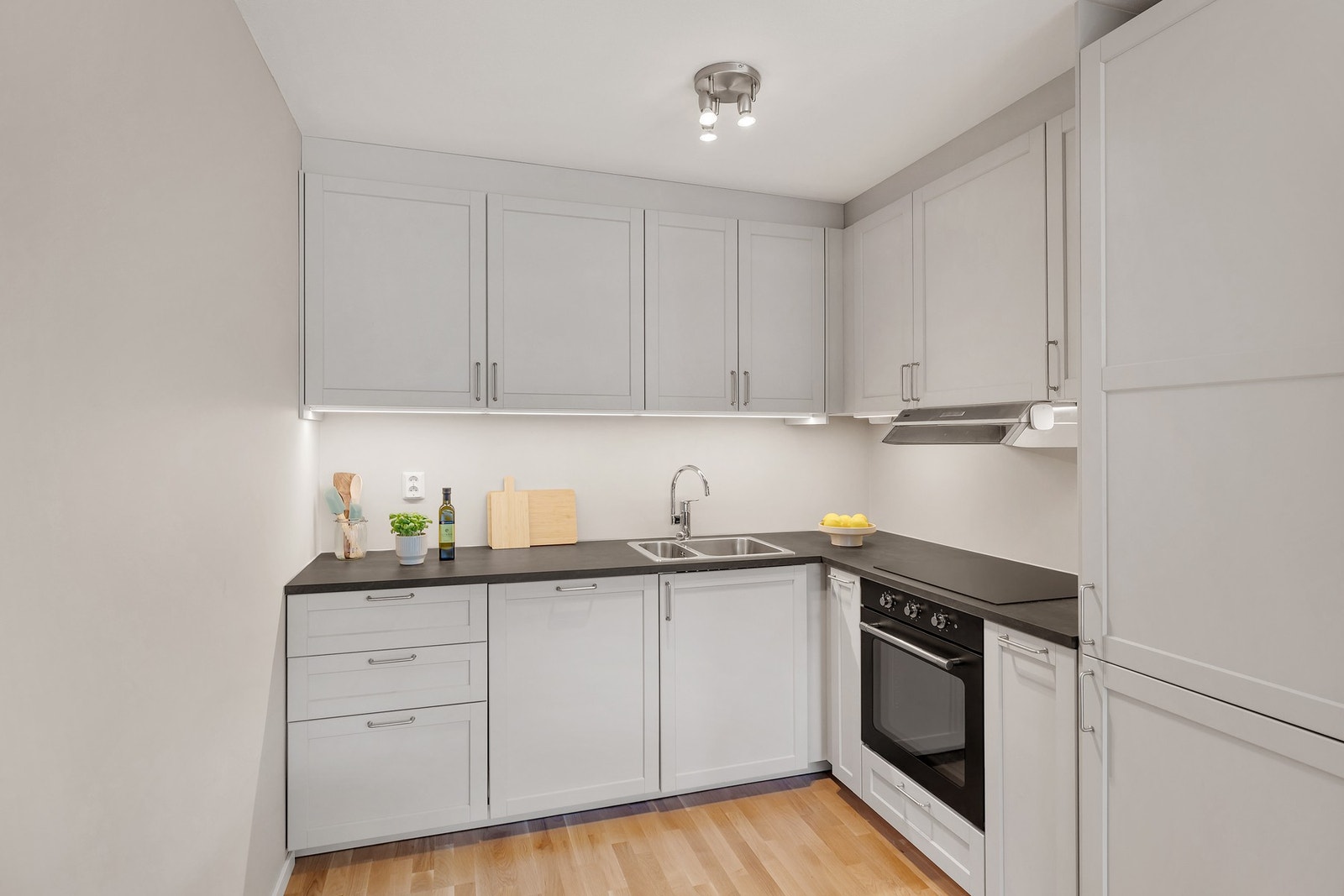 Kjøkkeninnredning fra IKEA med profilerte lakkerte fronter, laminat benkeplate, rustfri oppvaskkum, ventilator med utluft og innfelte
hvitevarer som stekeovn, induksjonsplatetopp, oppvaskmaskin og kombinert kjøle- og fryseskap. Galleribilde