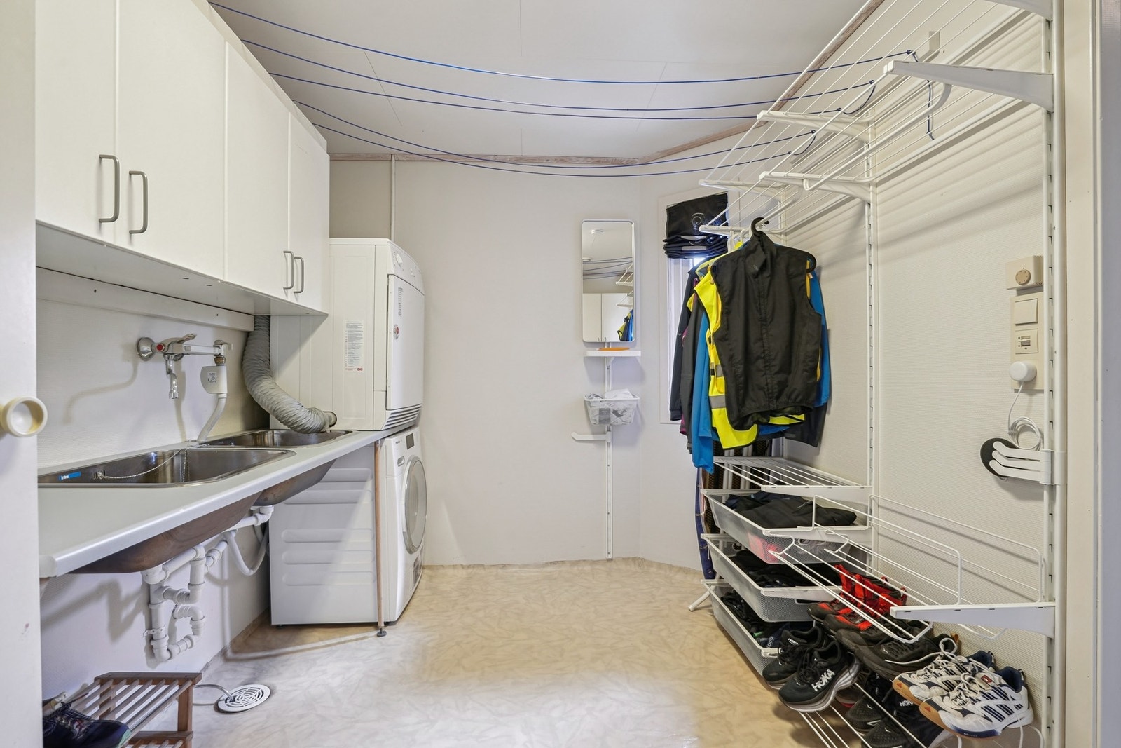 Praktisk vaskerom med vinylbelegg på gulvet og elektriske varmekabler. Innredet med laminat benkeplate med to stålskyllekummer, overskap, opplegg for vaskemaskin og tørketrommel. Galleribilde