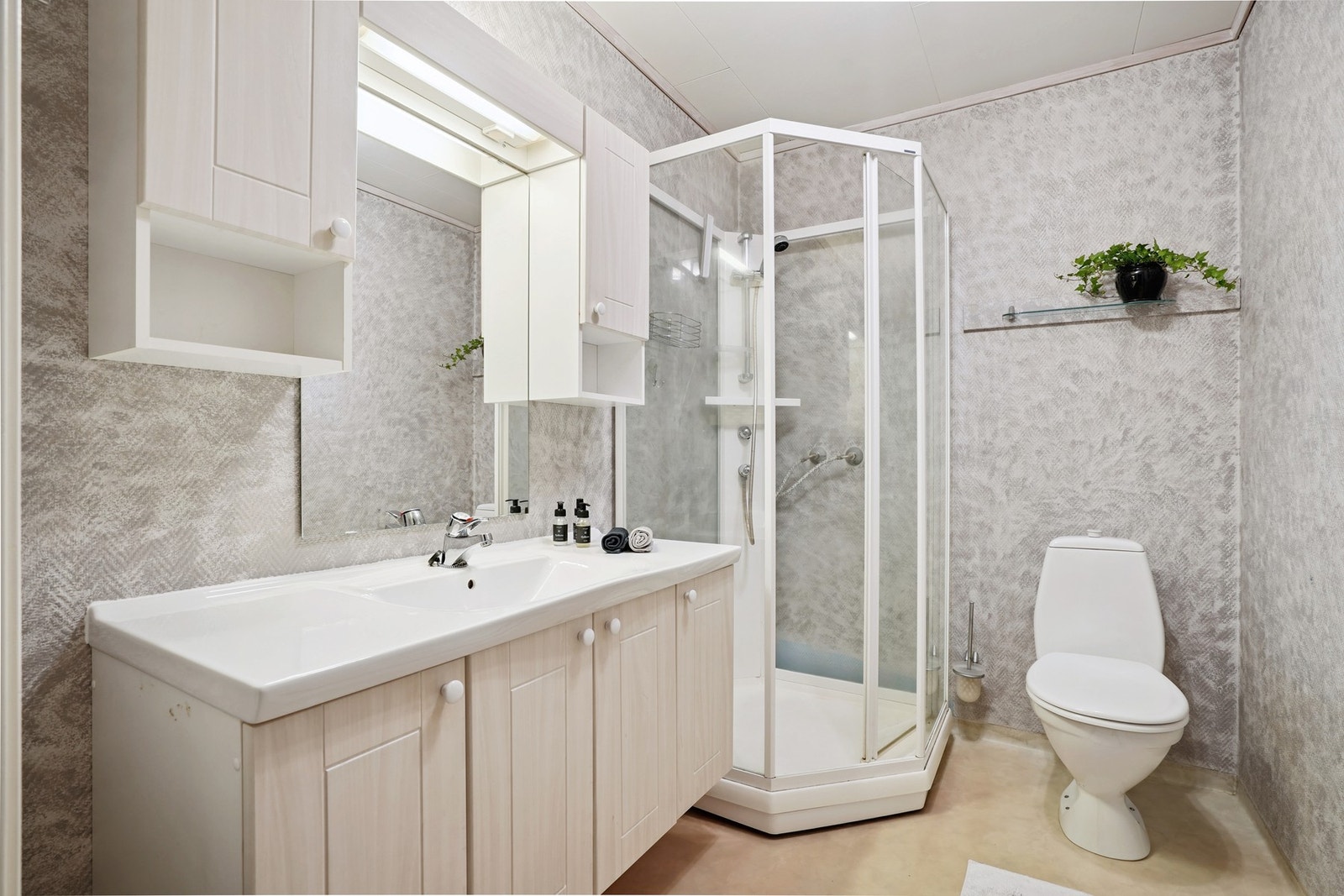 Badet har våtromstapet og vinylbelegg på gulvet med elektriske varmekabler. Innredet med baderomsinnredning, speil, overskap, dusjkabinett og toalett. Galleribilde