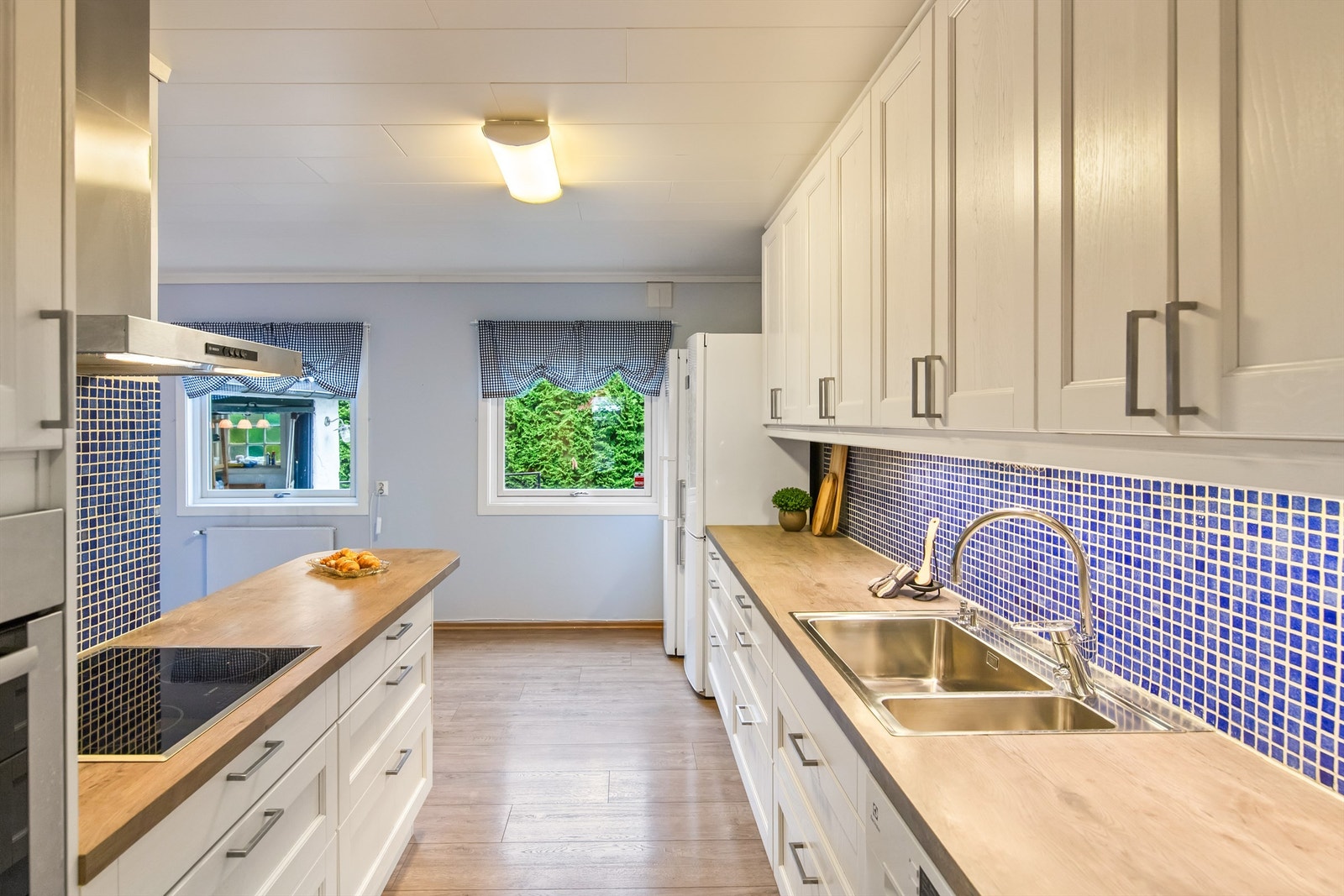 Kjøkkeninnredningen har hvite, profilerte fronter og benkeplater i laminat med nedfelt oppvaskkum. Fliser mellom overskap og benkeplass. Kjøkkenet har rikelig med skap- og benkeplass. Galleribilde