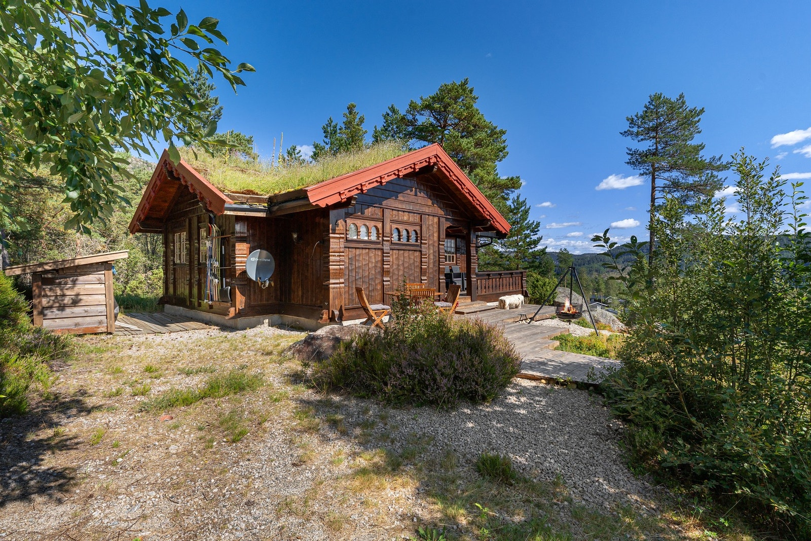Koselig trehytte med torvtak, veranda og bålplass, omgitt av skog og fjell. Galleribilde