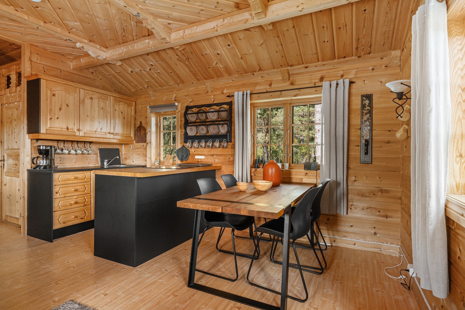 Åpent kjøkken og spiseplass i treverk med moderne, svart kjøkkenøy. Galleribilde