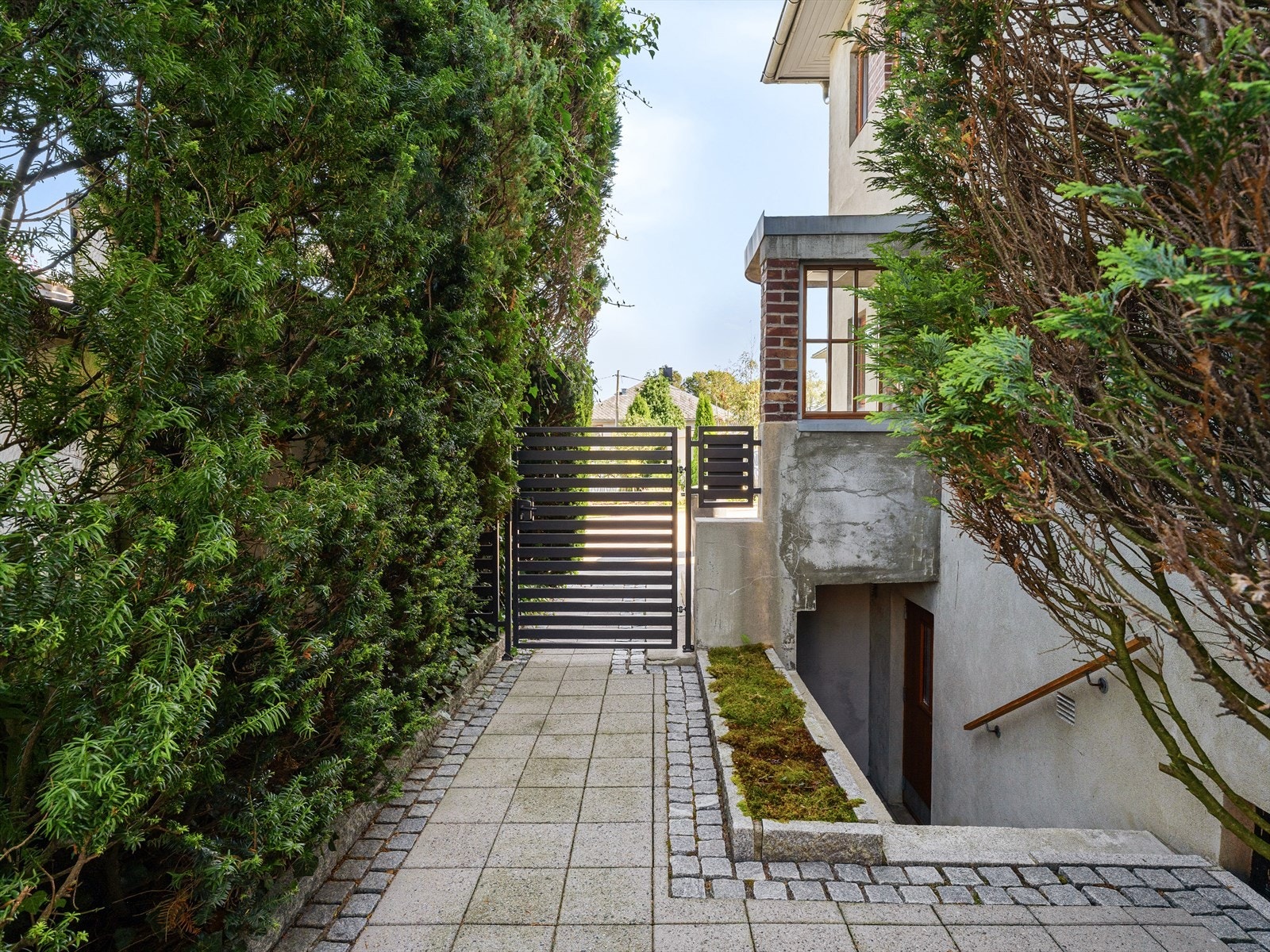 Port ved hovedinngang skjermer resten av eiendommen. Nedgang til kjelleretasjen, om ungdommen skal ha besøk. Innvendig trapp også. Galleribilde