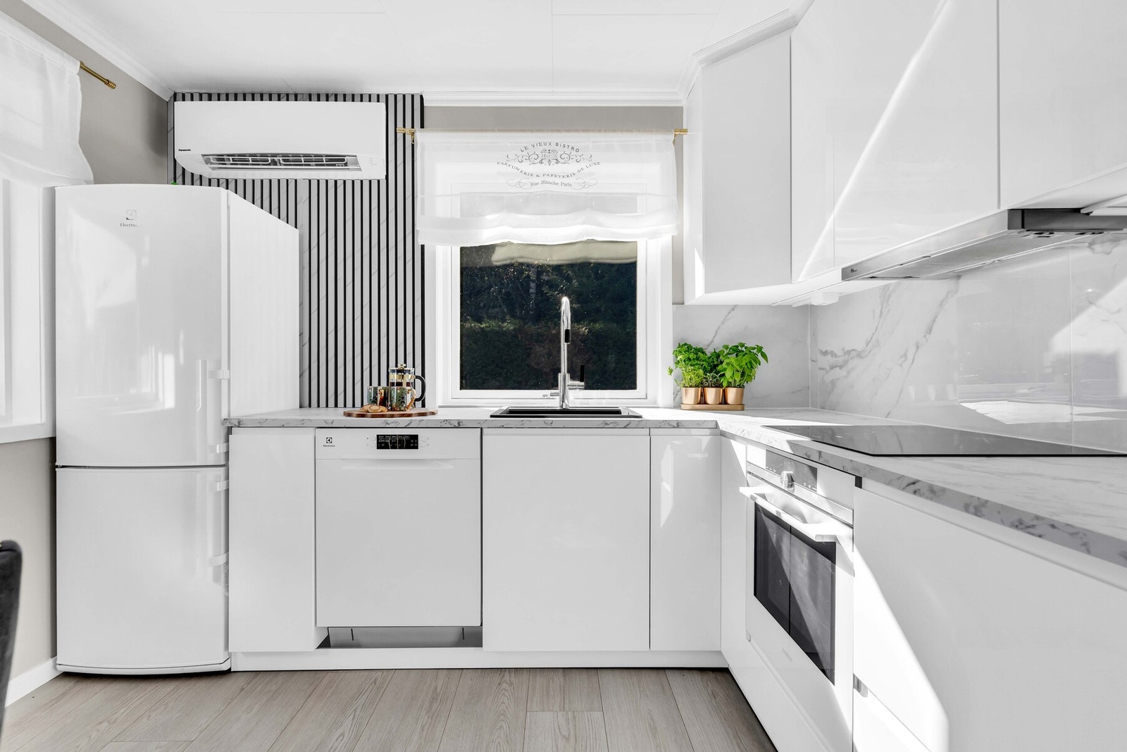 Leiligheten har en åpen kjøkkenløsning fra 2025 som gir rommet et friskt og moderne preg. Innredningen består av hvite høyglansfronter med laminert benkeplate, kombinert med fliser på veggen mellom benk og overskap - en tidløs og stilren løsning. Galleribilde