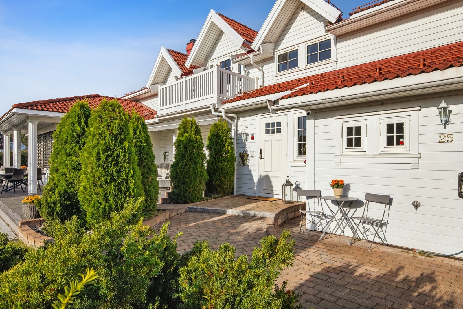 Solrikt inngangsparti med hyggelig sitteplass, omkranset av prydbusker og vintergrønne hekker. Galleribilde