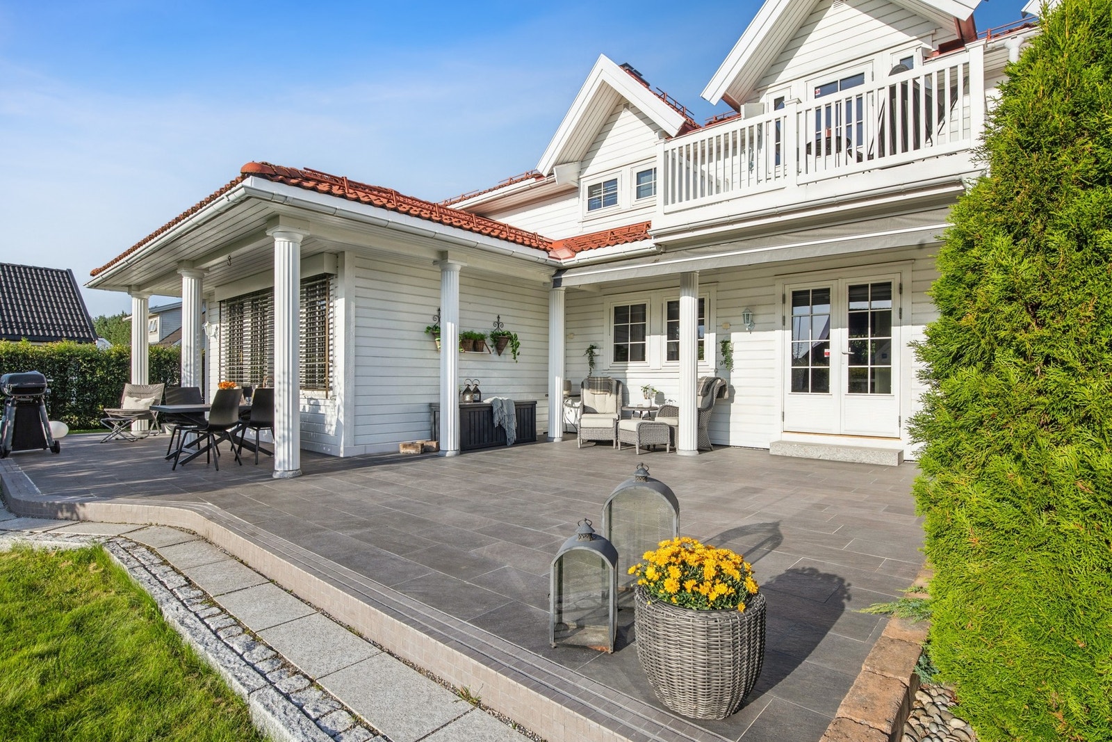 Lettstelt og skjermet uteplass med fliser, overbygget sitteområde og rom for både spisegruppe og lounge. Galleribilde