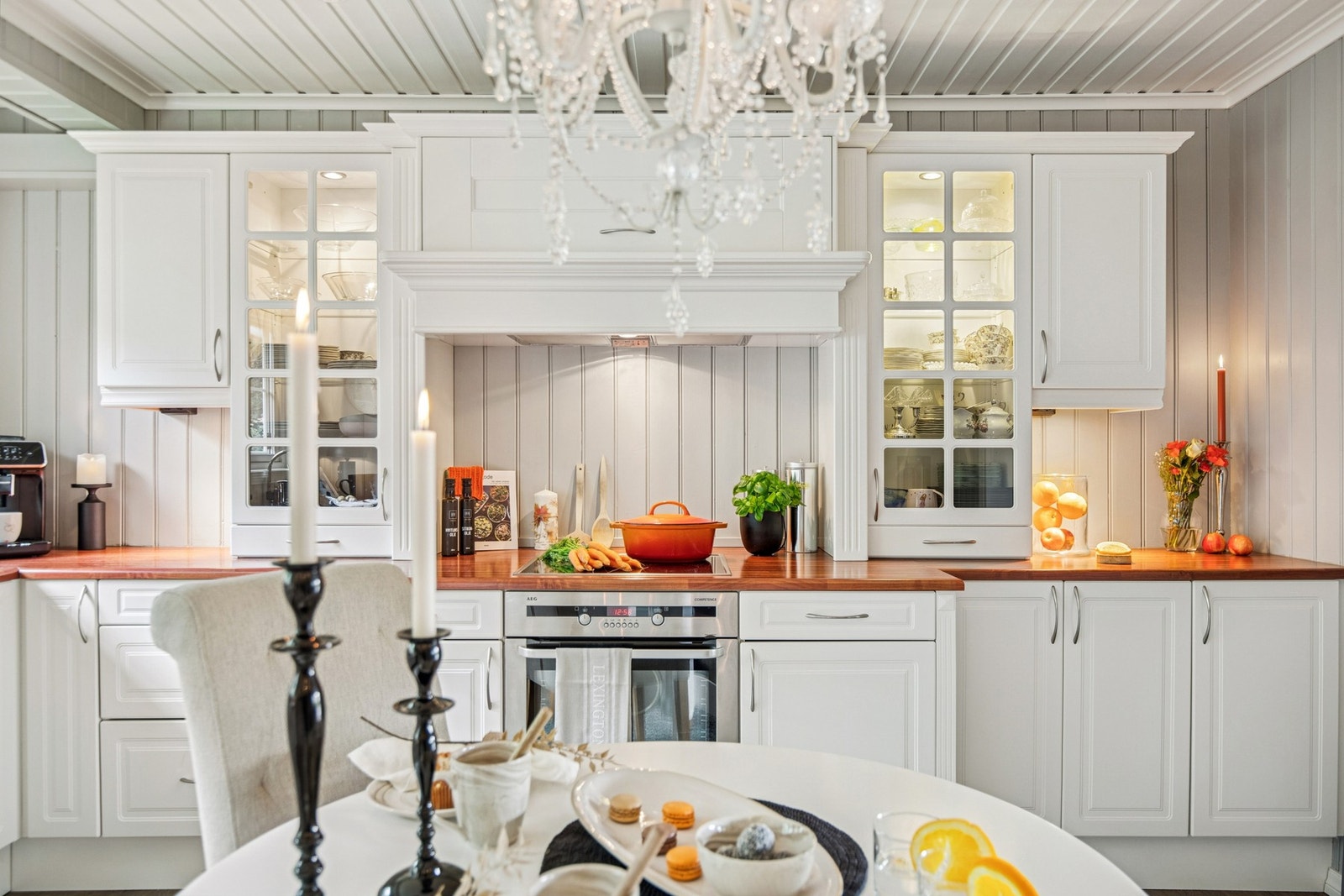 Klassisk kjøkkenløsning med benkeplater i tre, glassfronter i overskap med lys og plass til spisebord ved vinduene. Galleribilde