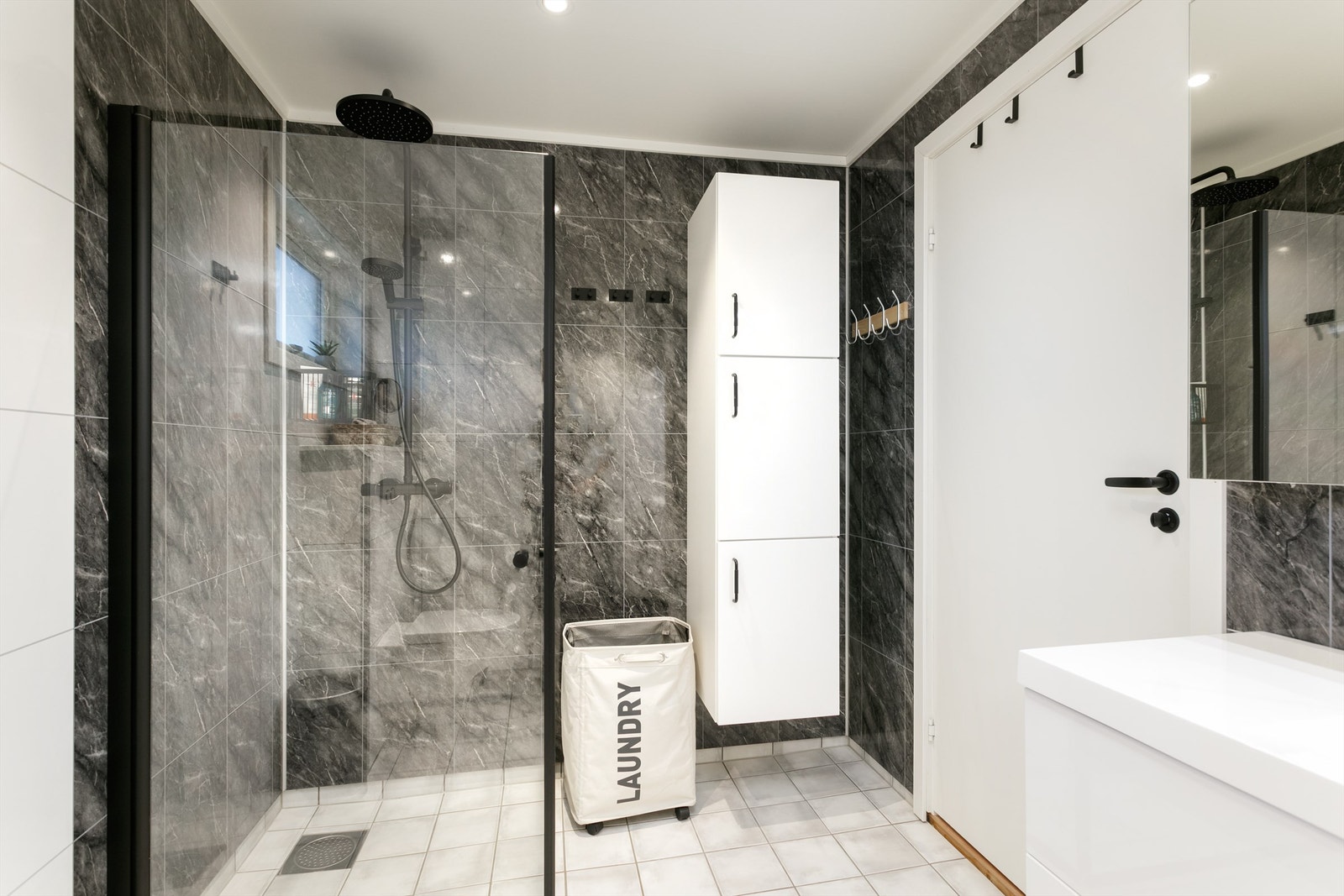 Bad i 1. etasje har innredning med skuffer og ovenpåliggende servant med sort ett-greps armatur. Speilskap med overlys og stikkontakt over servant. Dusjhjørne med glassvegger og sort vegghengt dusjarmatur med hånddusj og regndusj. Vegghengt toalett. Galleribilde