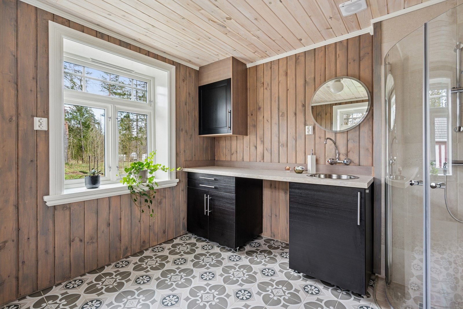 Rommet er innredet med en stor og moderne baderomsinnredning med skuffe- og skapseksjon, opplegg for vaskemaskin, speil på vegg, dusjsone med glassdør og toalett. Galleribilde