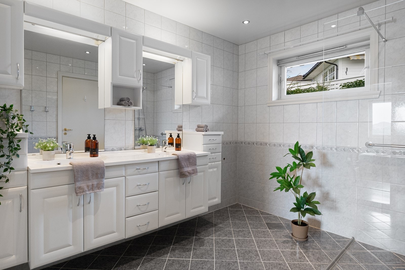 Badet er lyst og funksjonelt, innredet med servant med skap, overskap med speil/lys, dusjhjørne med glassvegger og gulvmontert toalett Galleribilde