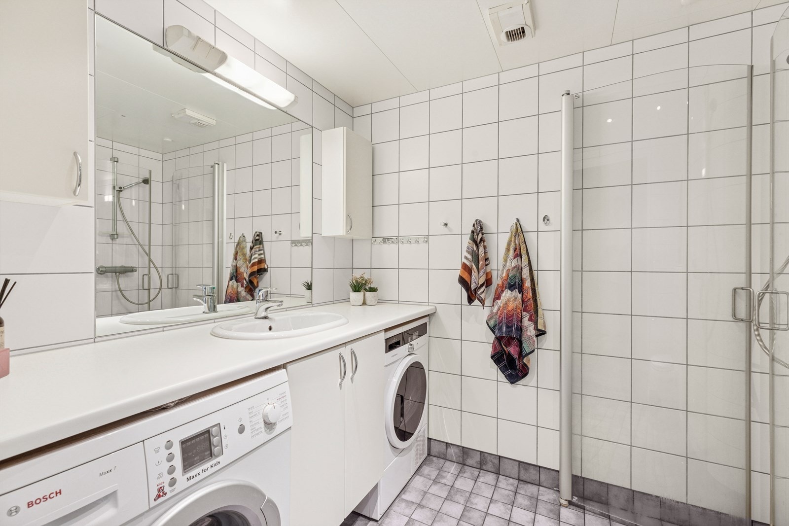 Pent baderom med langstående benkeplate, nedfelt servant og plass til både vaskemaskin og tørketrommel. Galleribilde