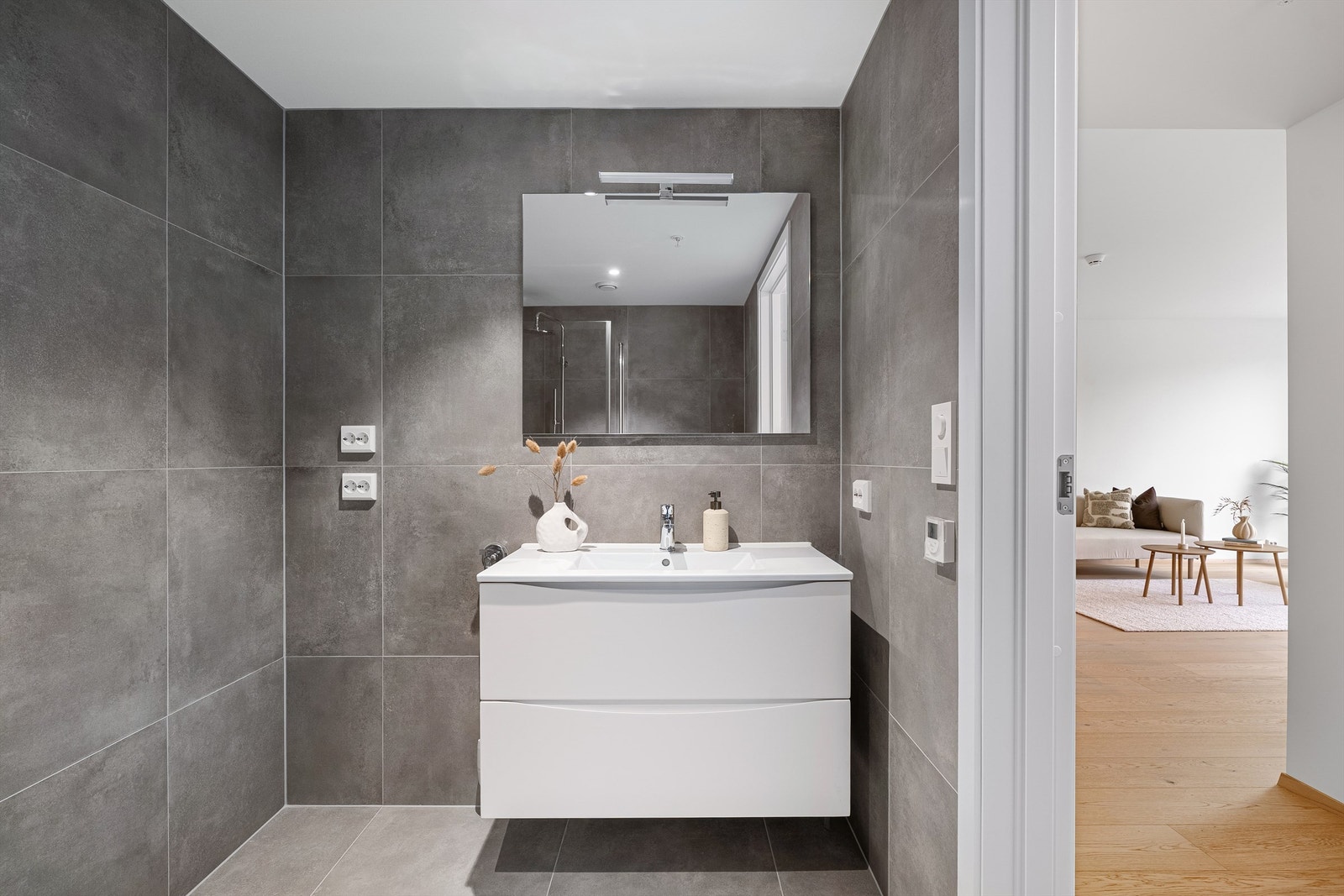 Badet er flislagt med moderne 60x60 fliser, og kan by på servant med oppbevaring samt opplegg til vaskemaskin og tørketrommel. Galleribilde