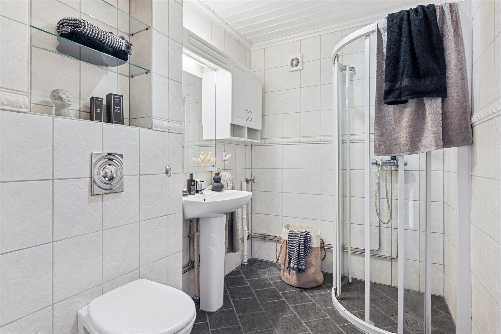 Badet inneholder søyleservant, vegghengt speil, vegghengt toalett, dusjhjørne med glassvegger og opplegg for vaskemaskin Galleribilde