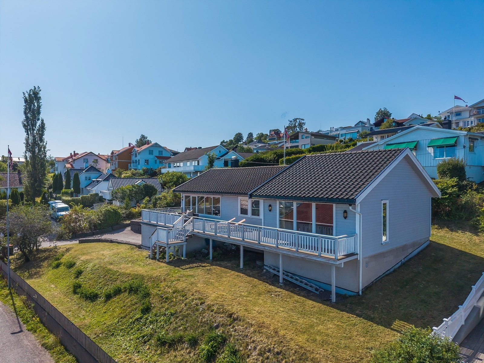 Fasade mot sjøen med stor veranda over hele bredden og med nedgang til hagen. Galleribilde