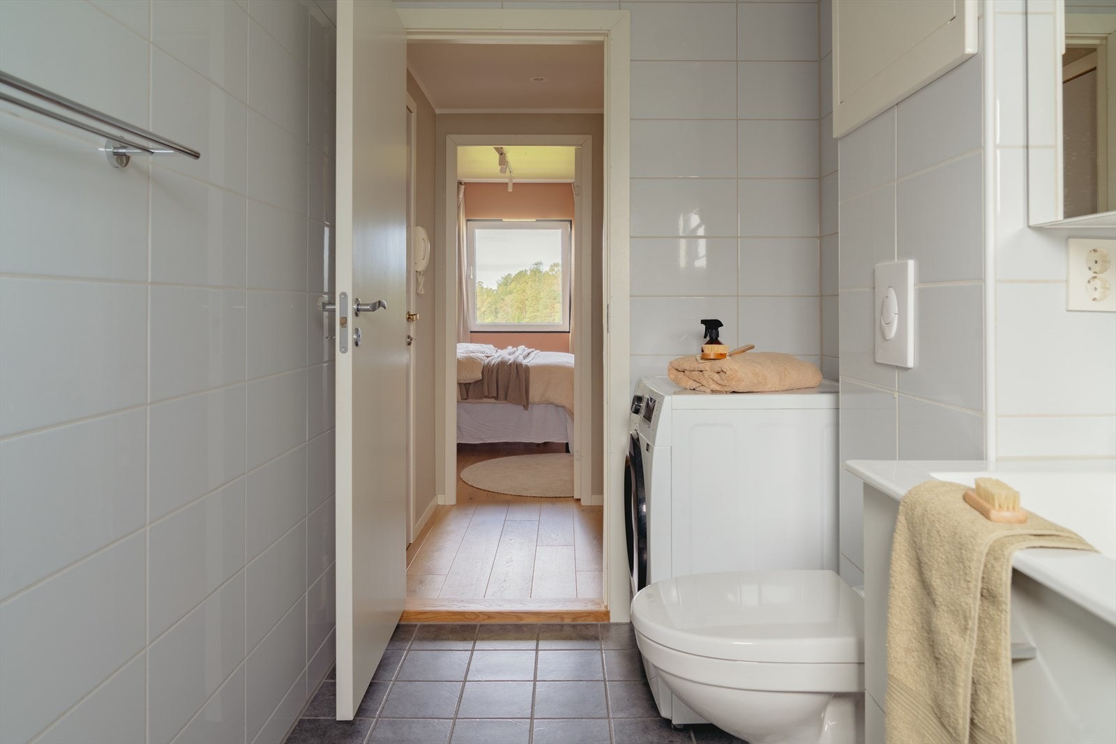 Badet er utstyrt med dusjvegger av glass og dusjgarnityr på vegg, vegghengt toalett, innredning med servant og opplegg for vaskemaskin Galleribilde