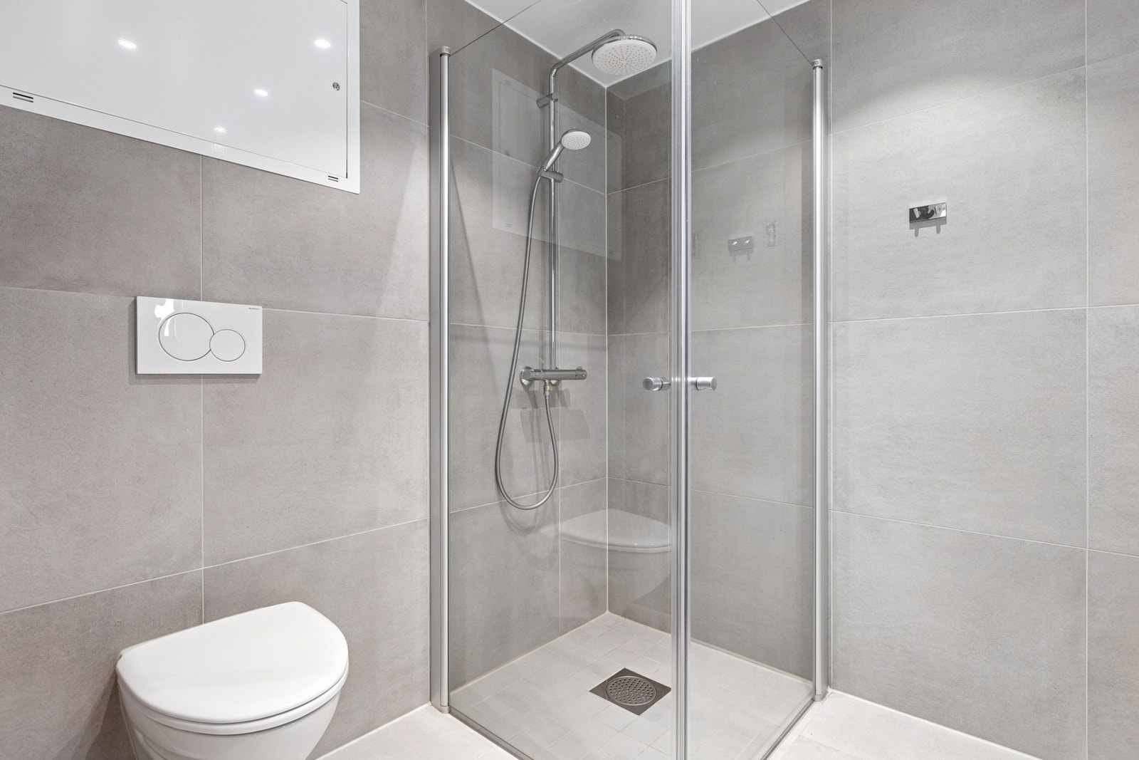 Badet er utstyrt med stor servantinnredning, speil med lys, dusjhjørne med innfellbare dusjdører og vegghengt toalett. Galleribilde