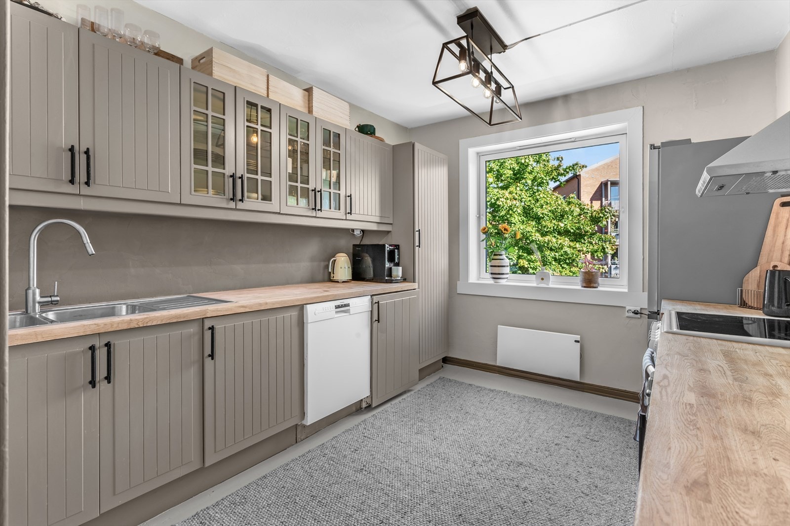 Hvitevarer som komfyr, oppvaskmaskin og kjøl/fryseskap. Vaskemaskin integrert i benkeskap. Lys under overskap. Stedvise overskapfronter med glass. Galleribilde