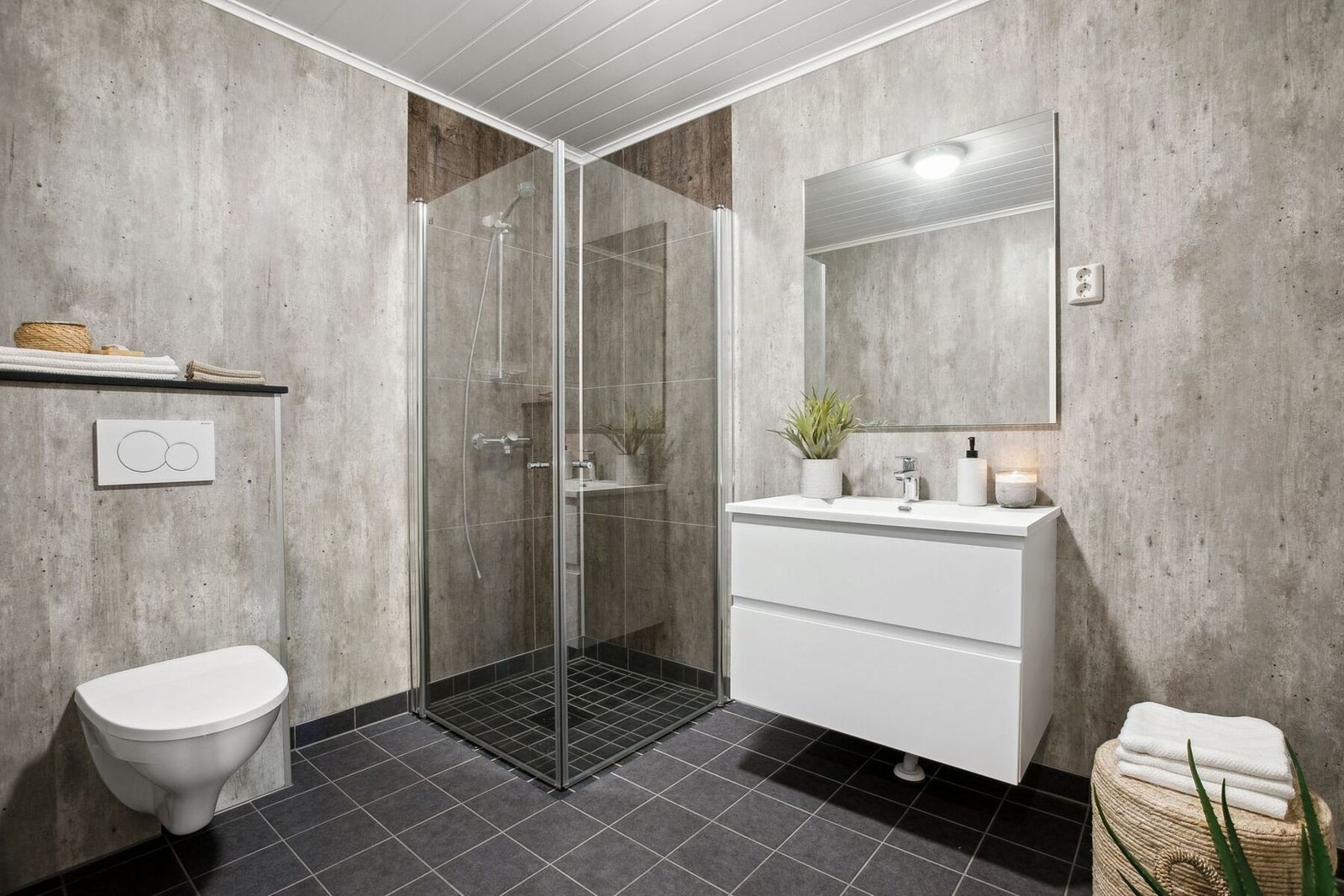 Badet har fliser på gulv og plater på veggene. Vegghengt toalett, baderomsinnredning mer servant og dusjhjørne med innfellbare glassdører finnes på badet. Galleribilde