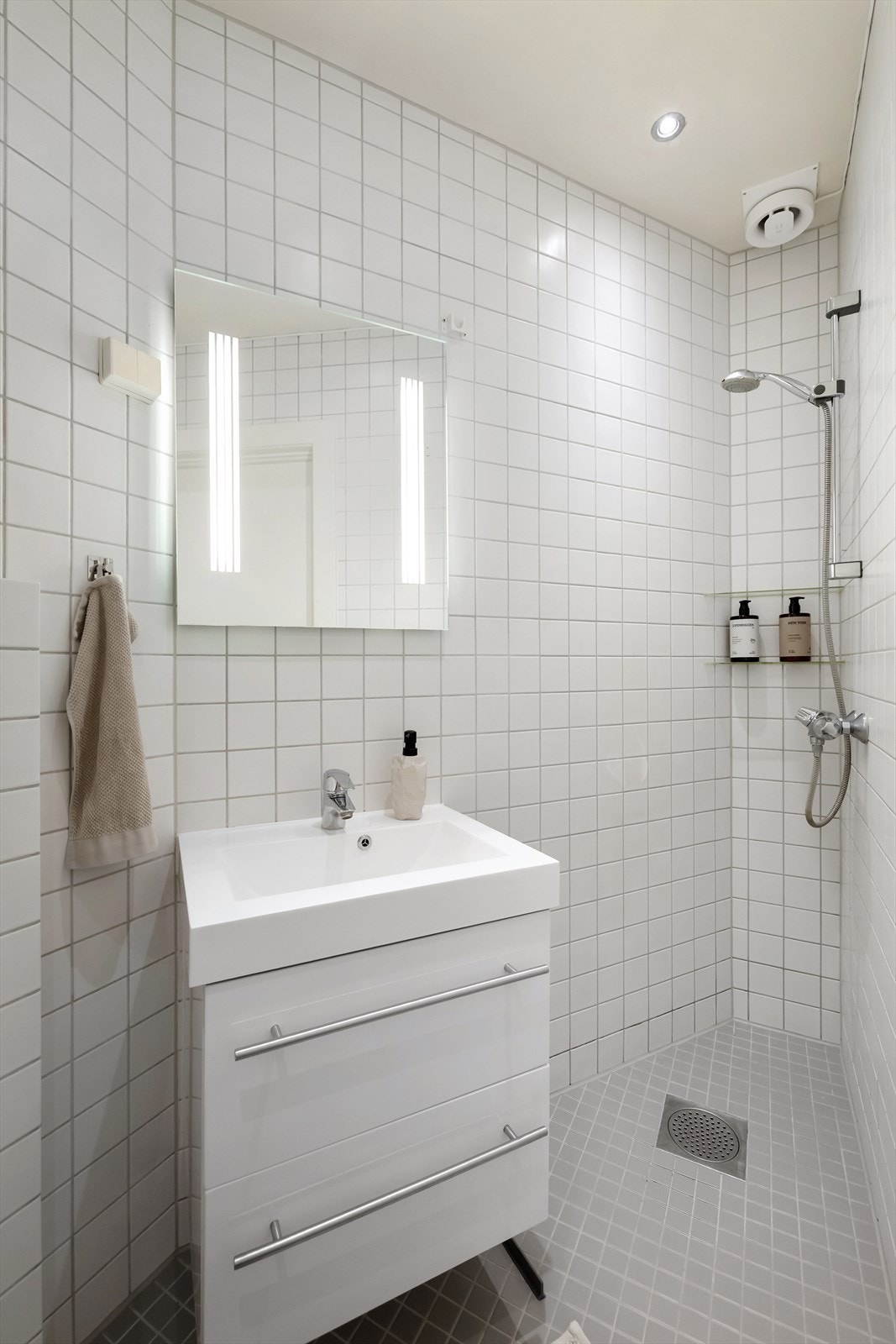 Baderomsinnredning med vegghengt servantskap med skuffer, ovenpåliggende servant og speil med belysning Galleribilde