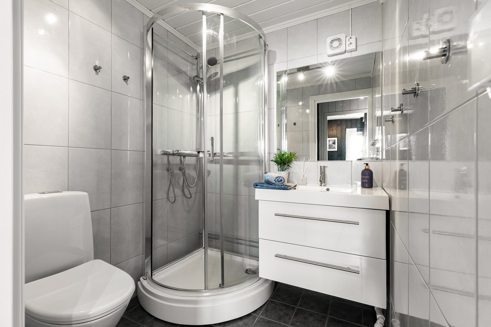 Badet har flislagte overflater på vegger og gulv. Dusjkabinett, innredning med nedfelt servant og underskuffer samt toalett Galleribilde