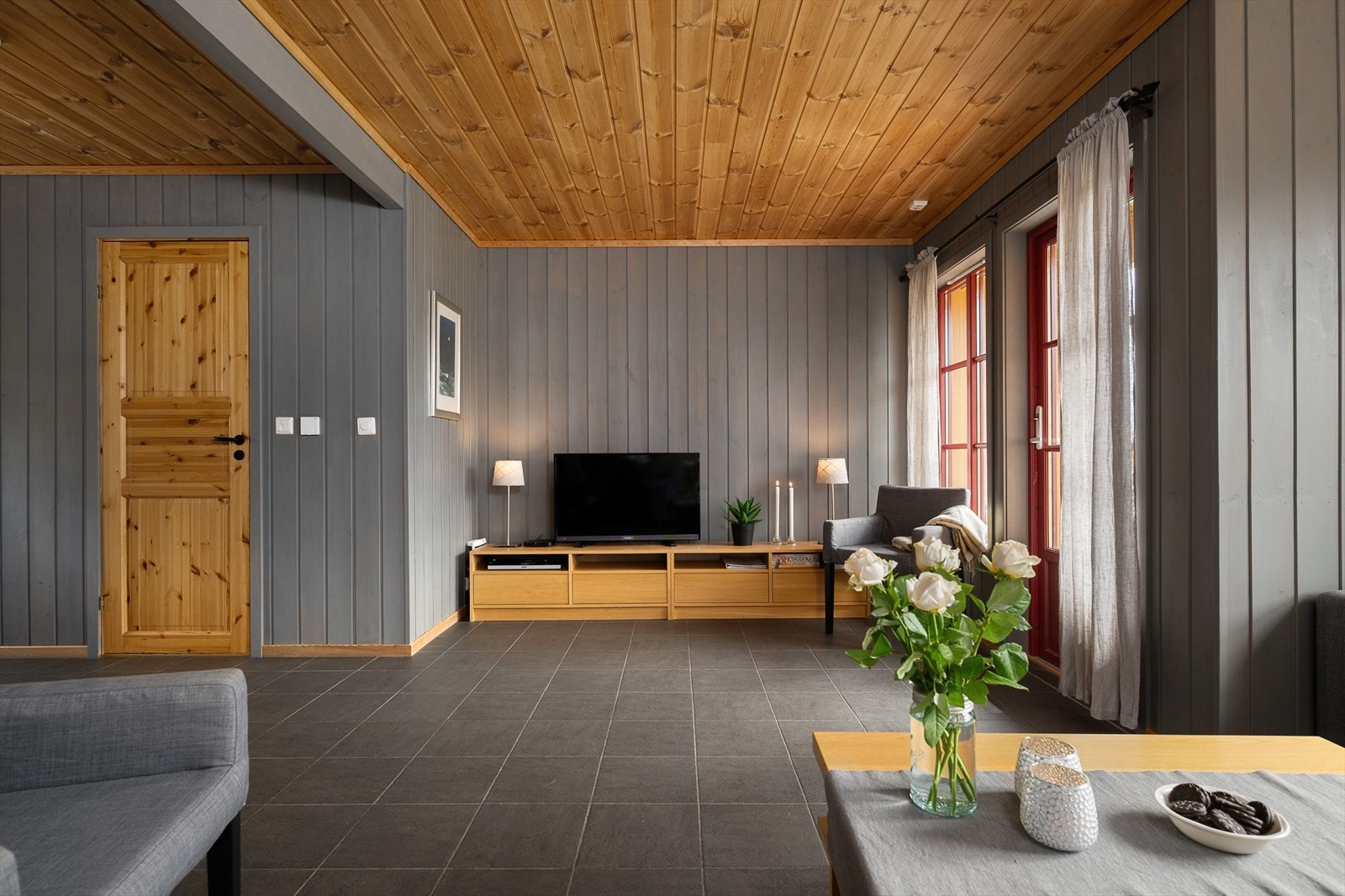 Romslig og koselig stue med TV-krok, moderne gråtoner på veggene, og store vindusflater som slipper inn rikelig med dagslys. Galleribilde