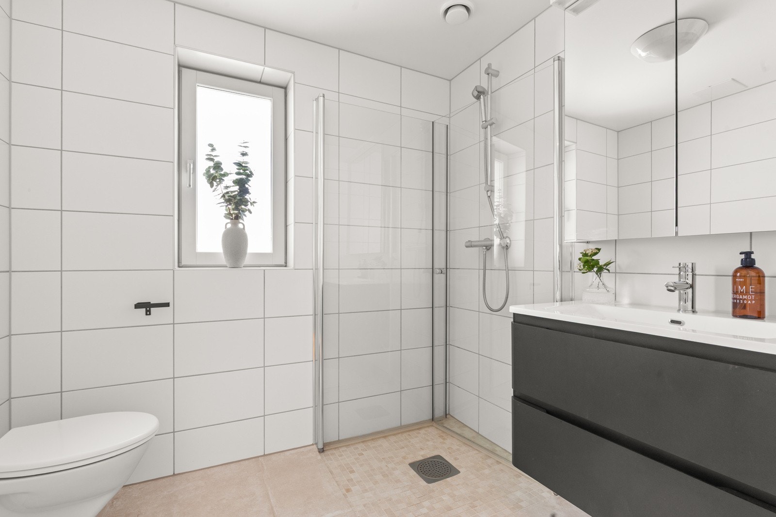 Lyst og delikat baderom utstyrt med servantinnredning, speilskap, vegghengt toalett og dusjhjørne med innfellbare glassdører. Behagelig varme i gulv. Galleribilde