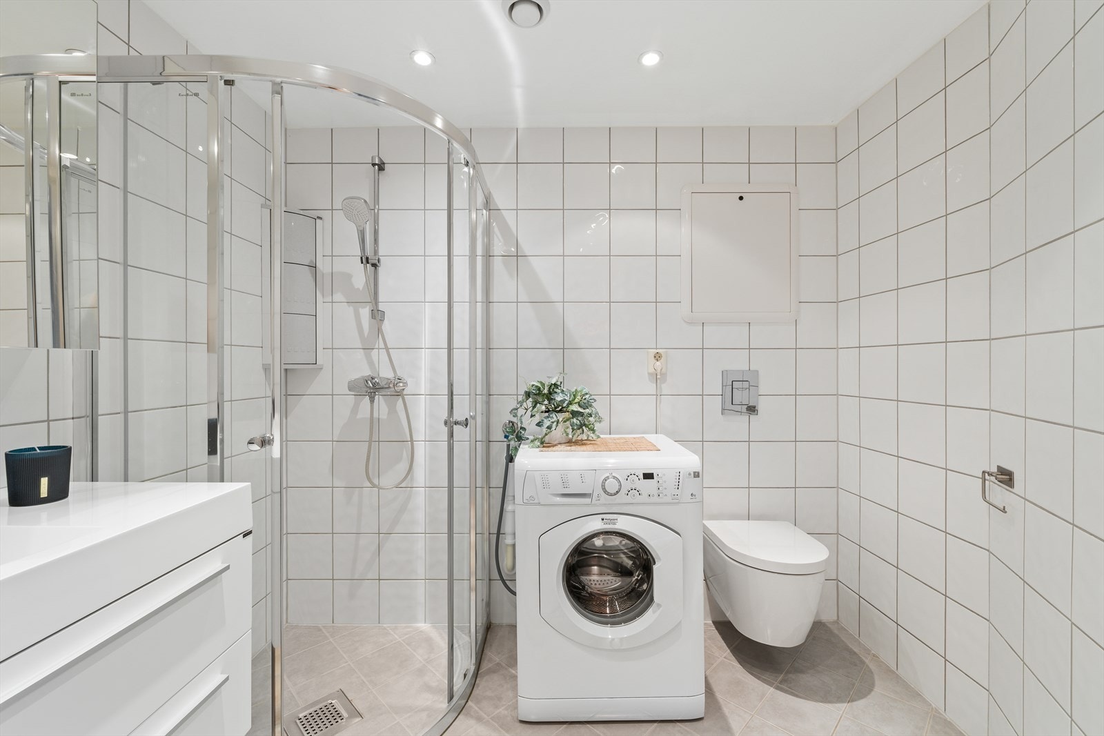 Badet er innredet med veggmontert toalett, dusjvegger/hjørne, innredning med nedfelt servant samt opplegg for vaskemaskin Galleribilde