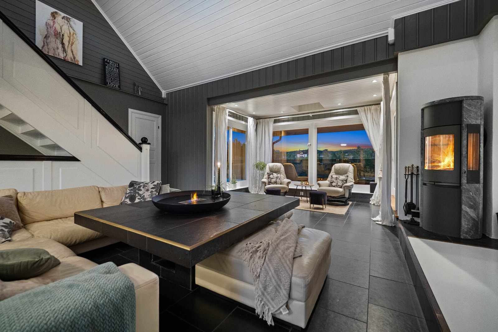 I denne luftige stuen med 6,4 meter under taket og en varm klebersteinsovn, er det bare å skru ned lyset for å skape kino. Blir ikke dette drømmerommet for hele familien? Galleribilde