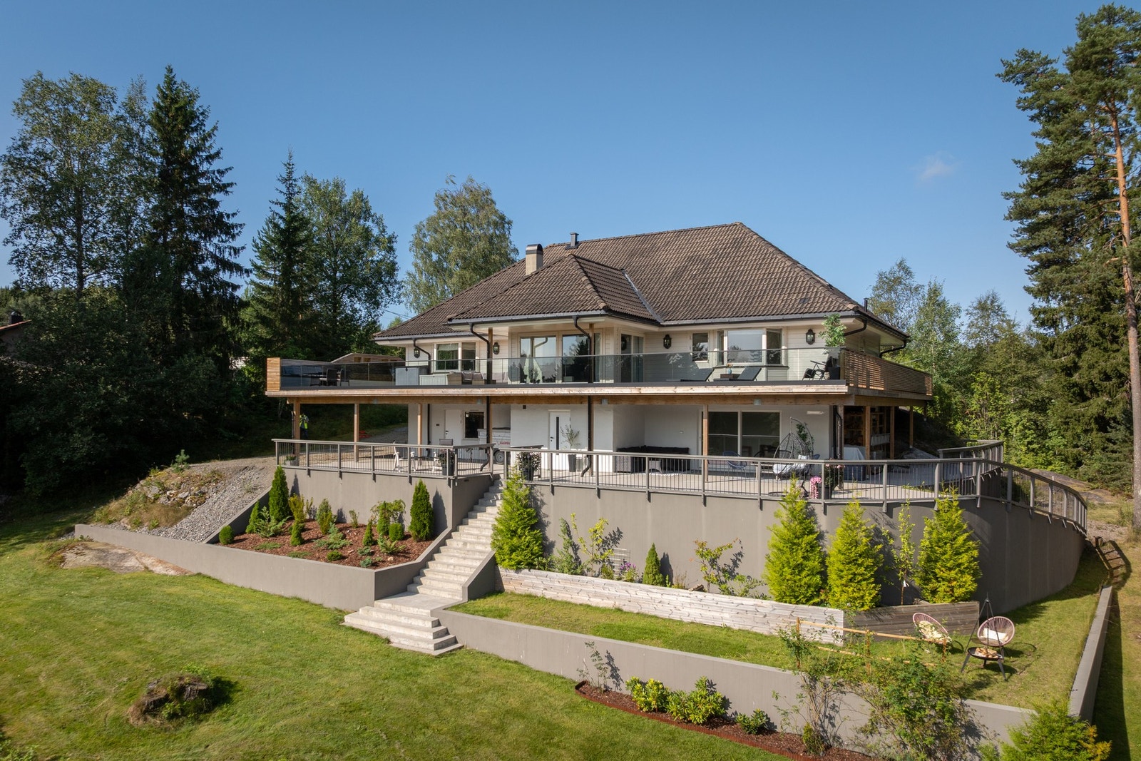 Villaen har støttemurer med terrasserte bed, velstelt beplantning og innfelte spotter for stemningsfull belysning. Galleribilde