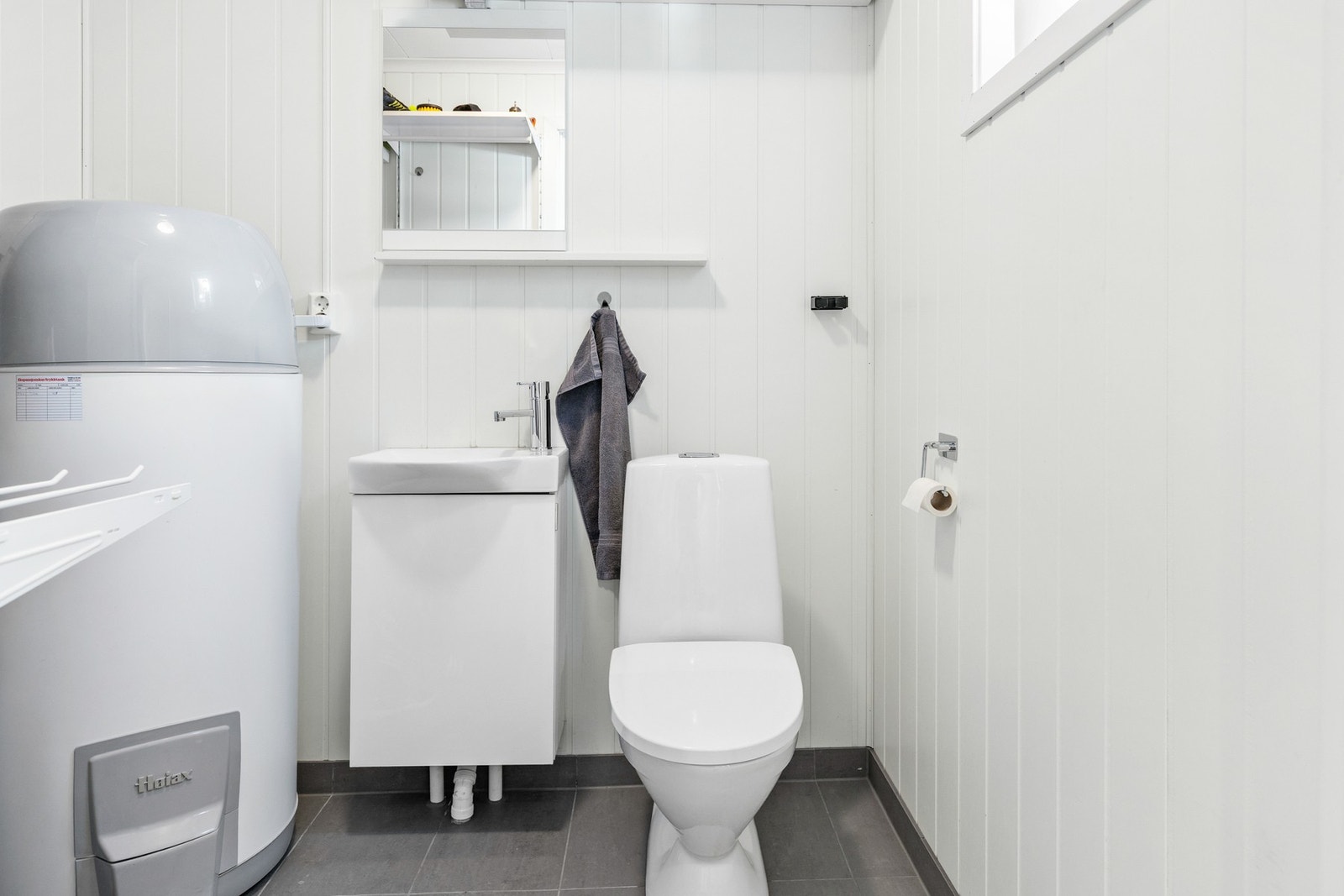 Separat toalettrom innredet med gulvmontert toalett, servant i innredning med speil og varmtvannsbereder Galleribilde